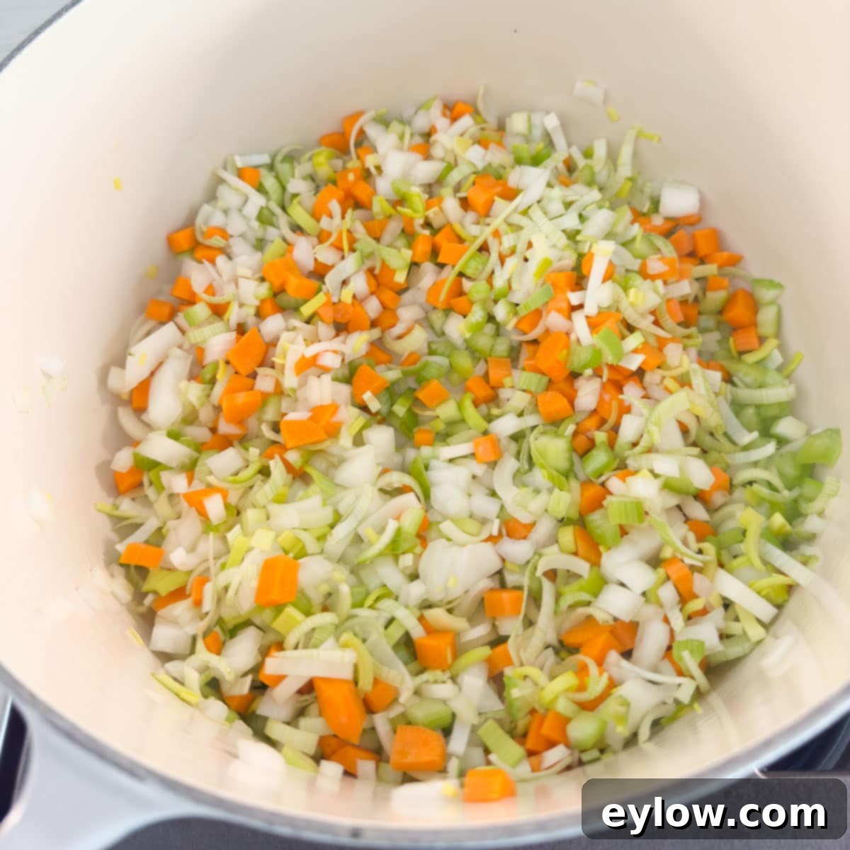 Chopped carrots, celery, onion, and leek simmering gently in olive oil within a large soup pot.