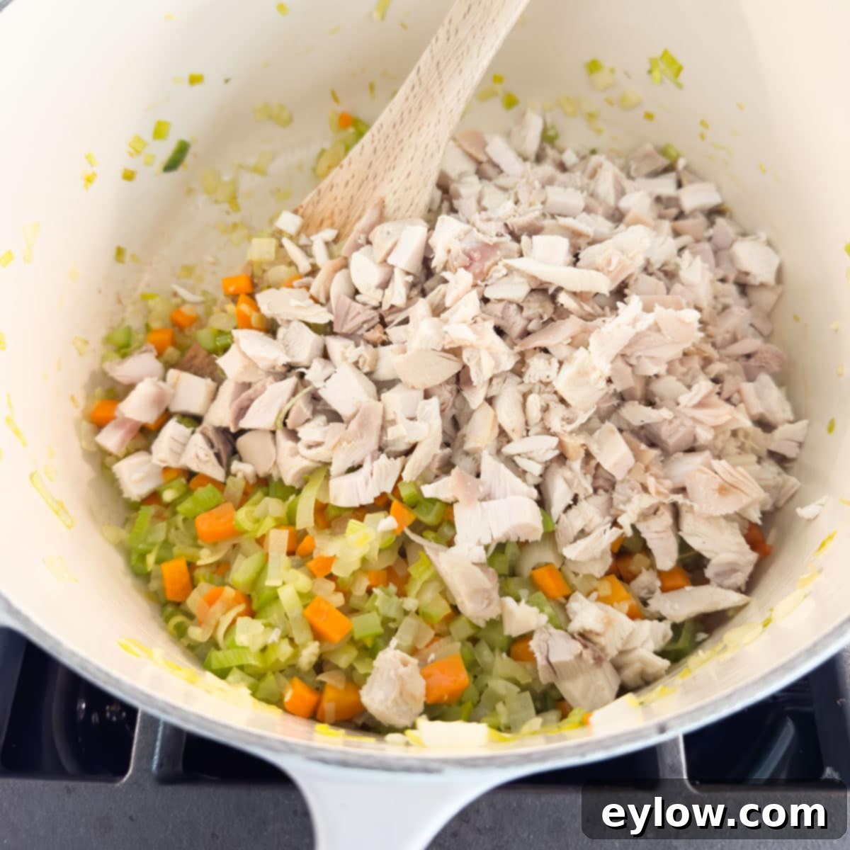 Adding savory chopped turkey pieces to the sautéed vegetables in a large soup pot, stirring with a wooden spoon.
