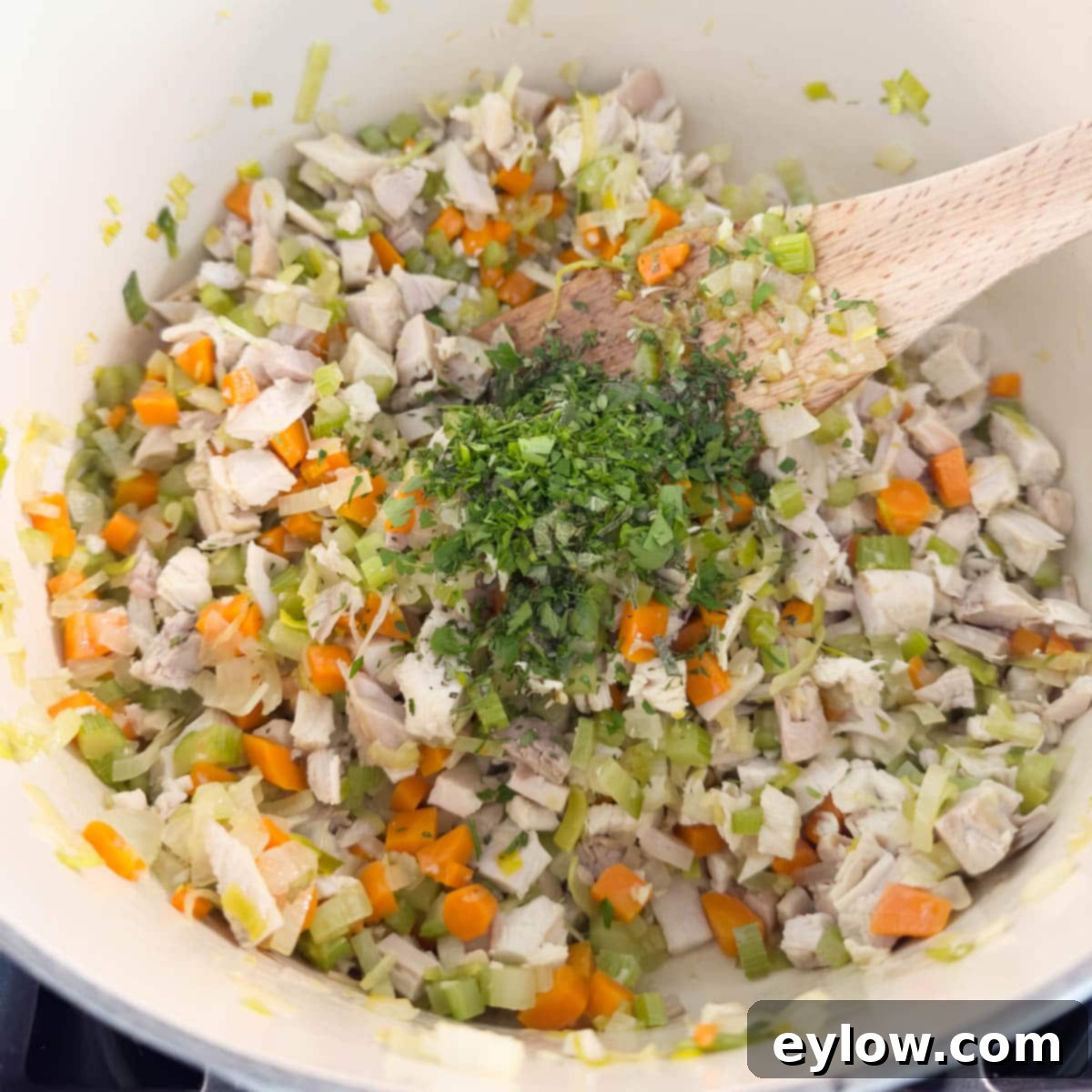 Stirring vibrant chopped fresh green herbs, including thyme and parsley, into a simmering pot of turkey soup.