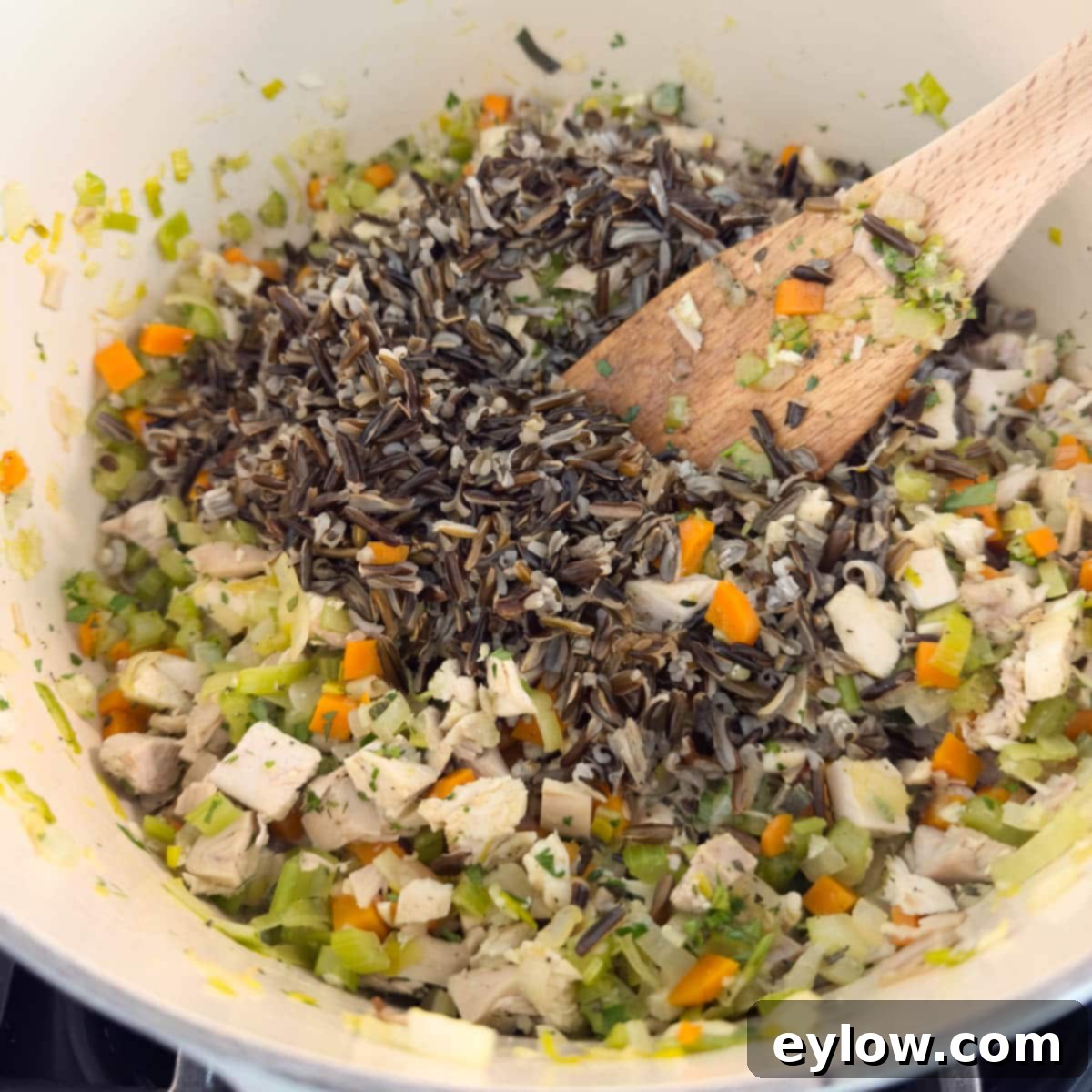 Adding pre-cooked wild rice to a pot of turkey soup with vegetables and herbs, ready for simmering.