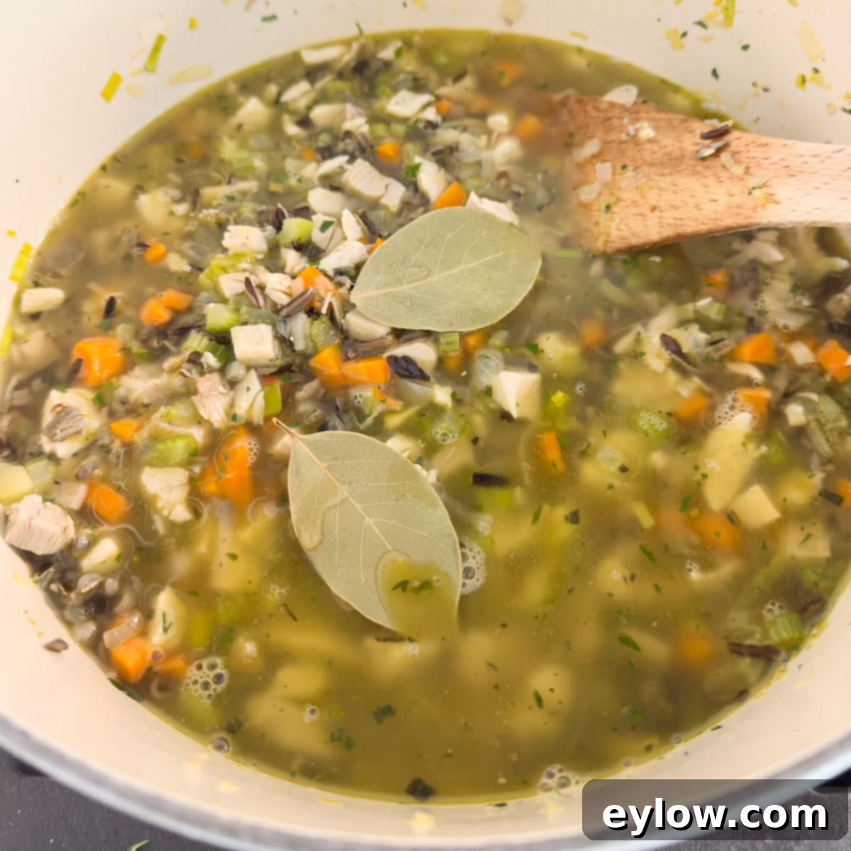 Bay leaves simmering in a pot of turkey and wild rice soup, blending their aromatic qualities with the vegetables and meat.