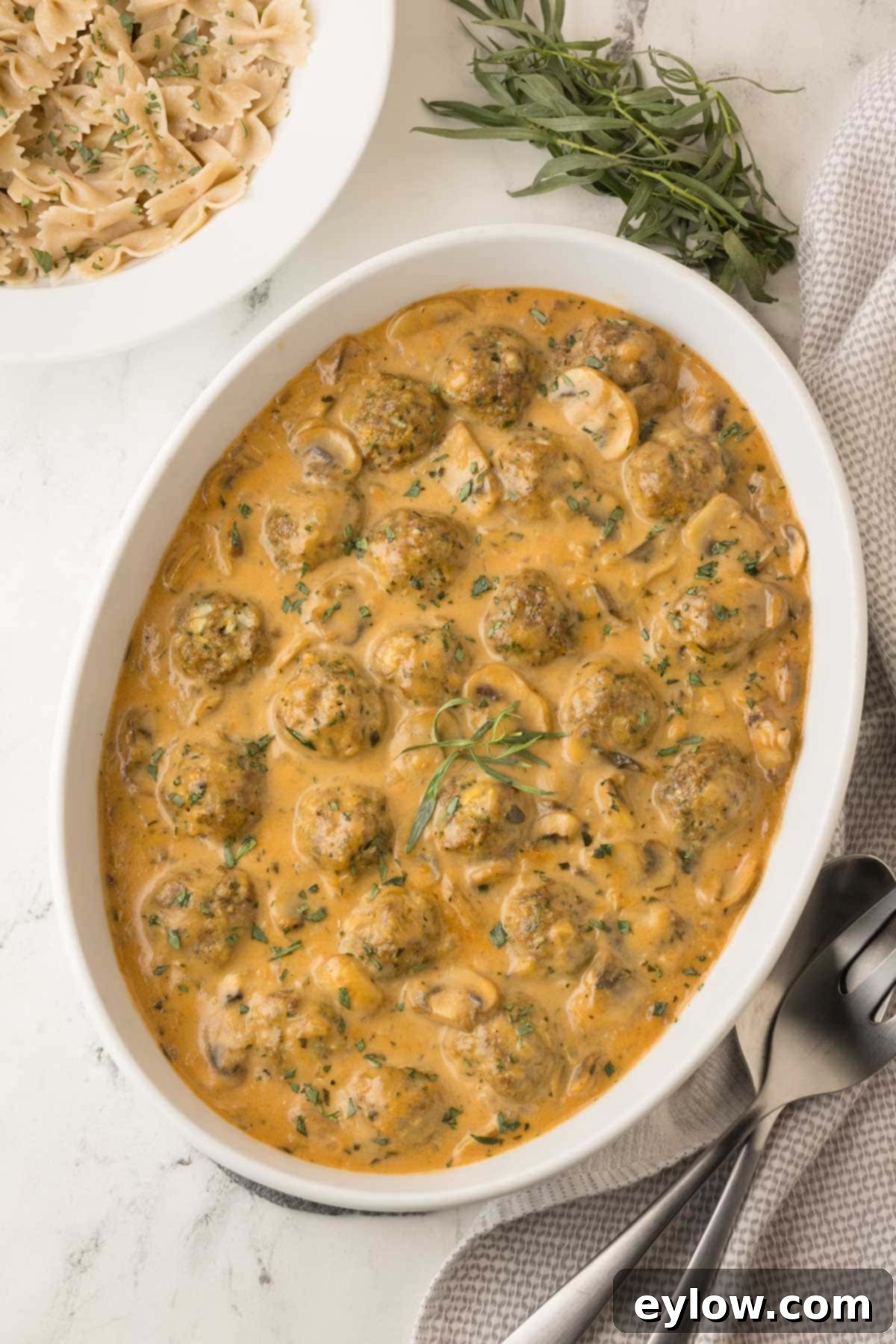 White oval casserole dish with creamy meatball beef stroganoff topped with fresh tarragon.