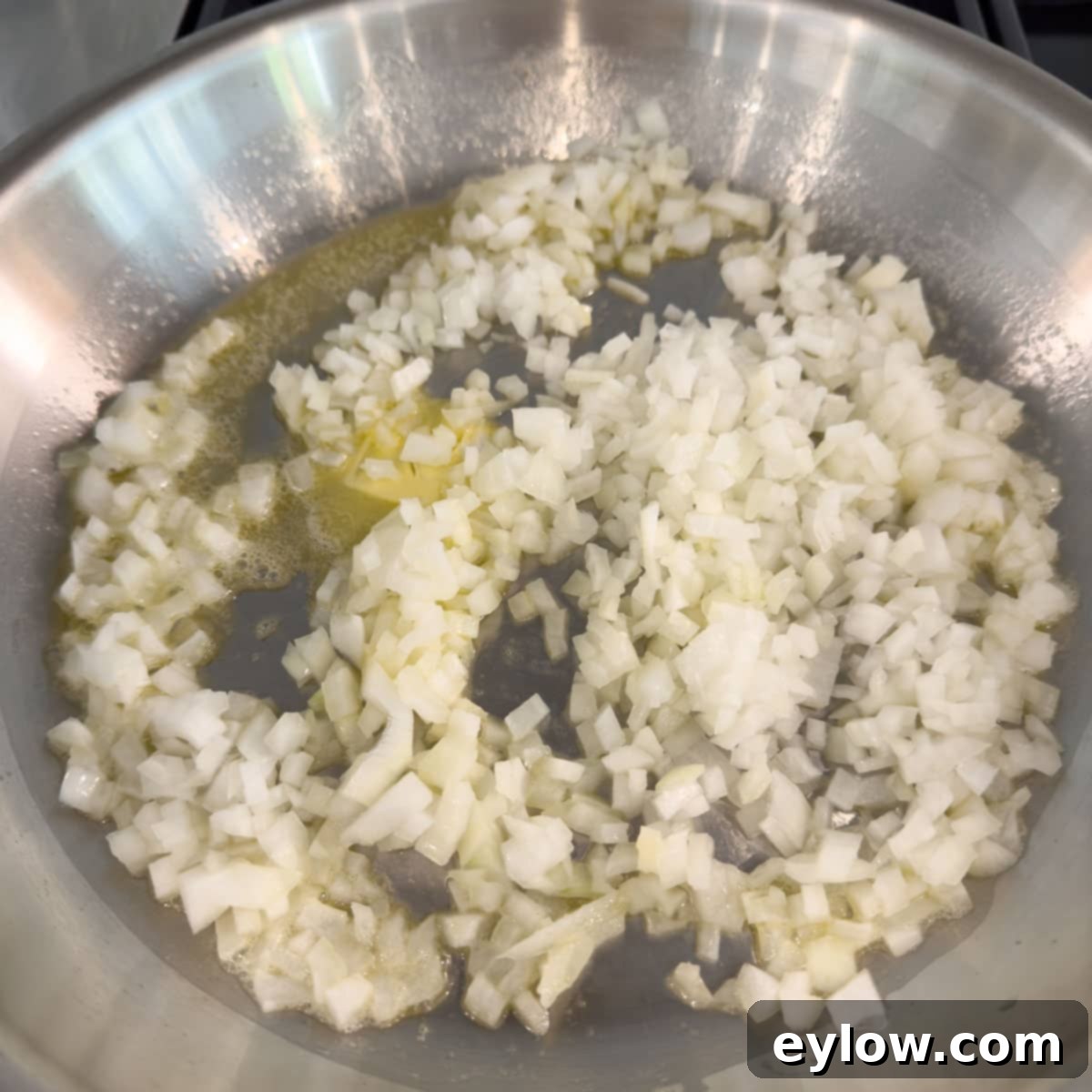 Chopped onions sautéing in butter in a stainless steel fry pan.