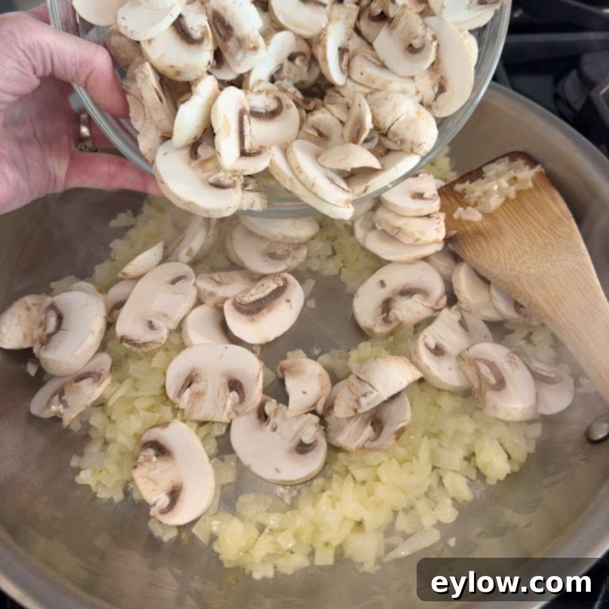 Adding sliced mushrooms to a pan of sautéed onions in butter.