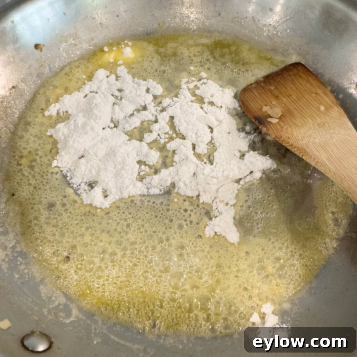 Melted butter and flour cooking in a steel pan with a wooden spatula.