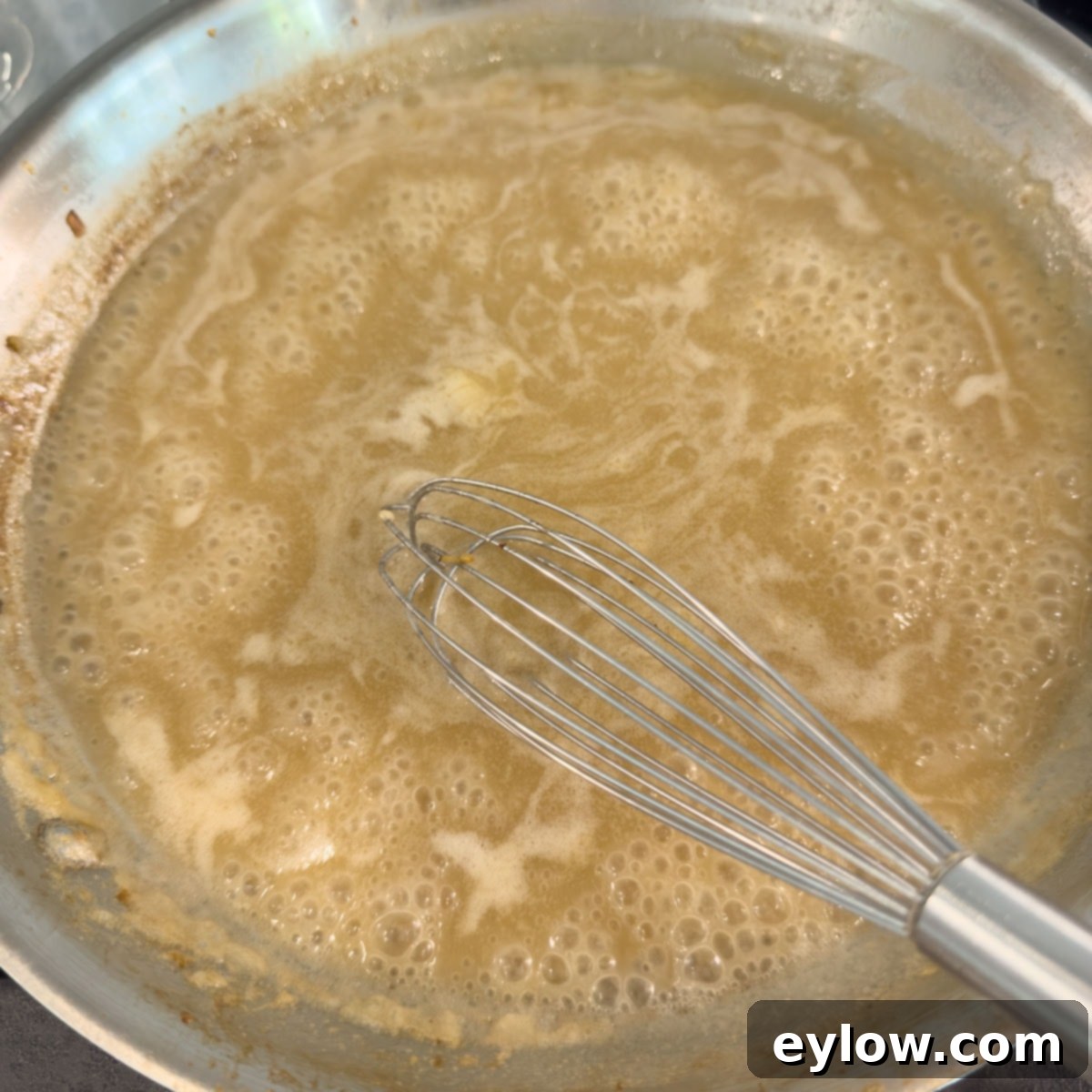 A golden bubbly sauce with a steel whisk in a saute pan.