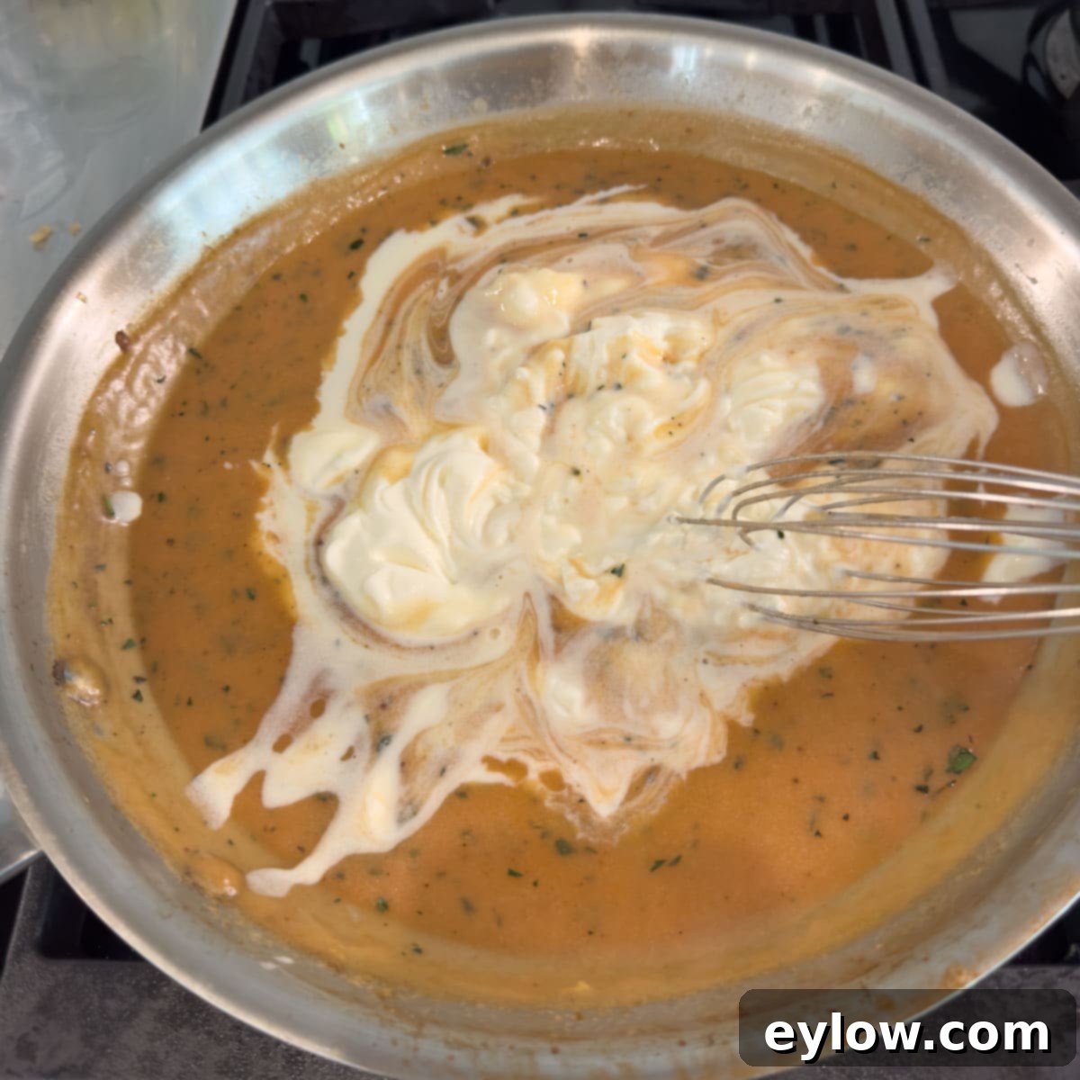Creme fraiche being added to a pan with stroganoff sauce and a wire whisk.
