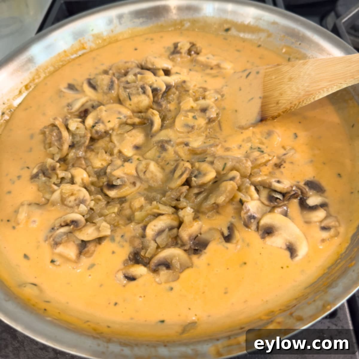 Mushrooms added to stroganoff sauce in a saute pan with a wooden spatula.