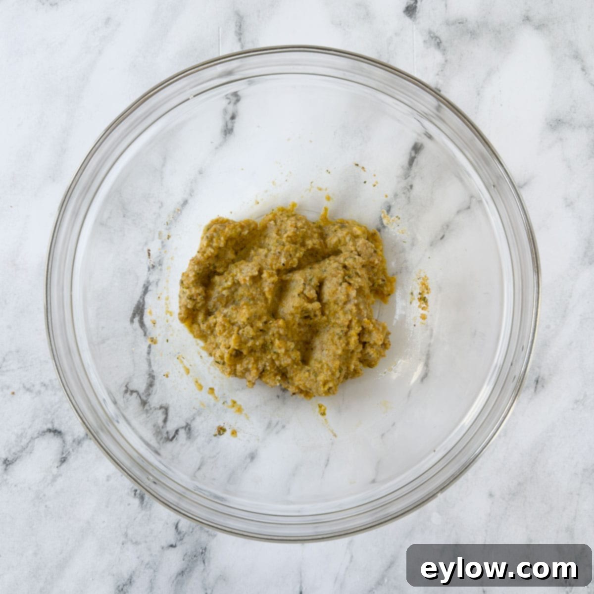 A glass bowl with breadcrumbs, herbs, and egg to make a meatball binder. 