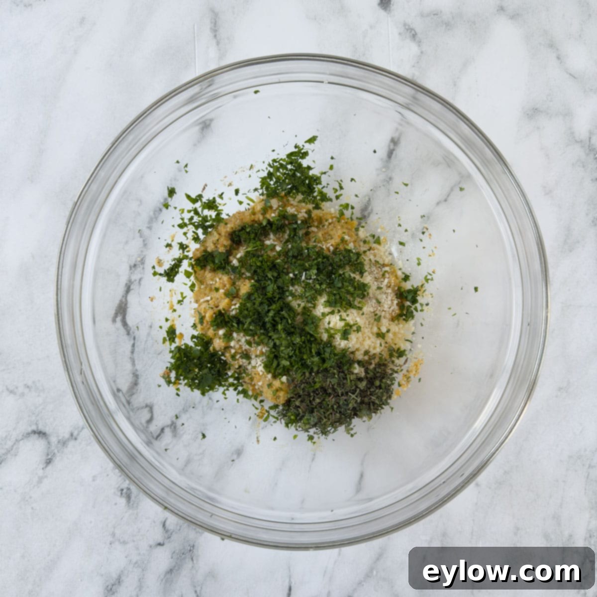 A meatball breadcrumb mix with herbs added in a glass bowl.
