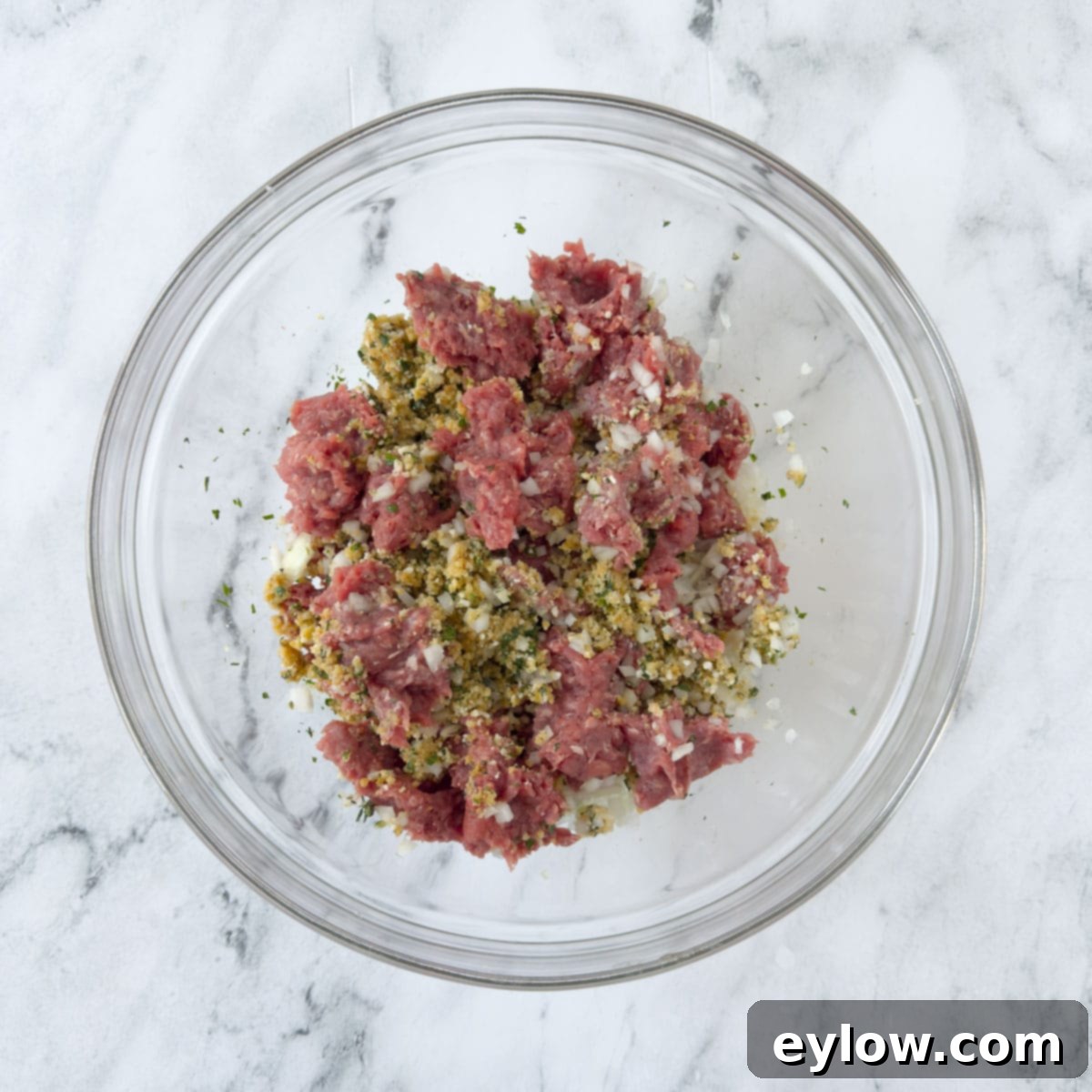 Adding pink ground beef to a bowl making meatball mix.