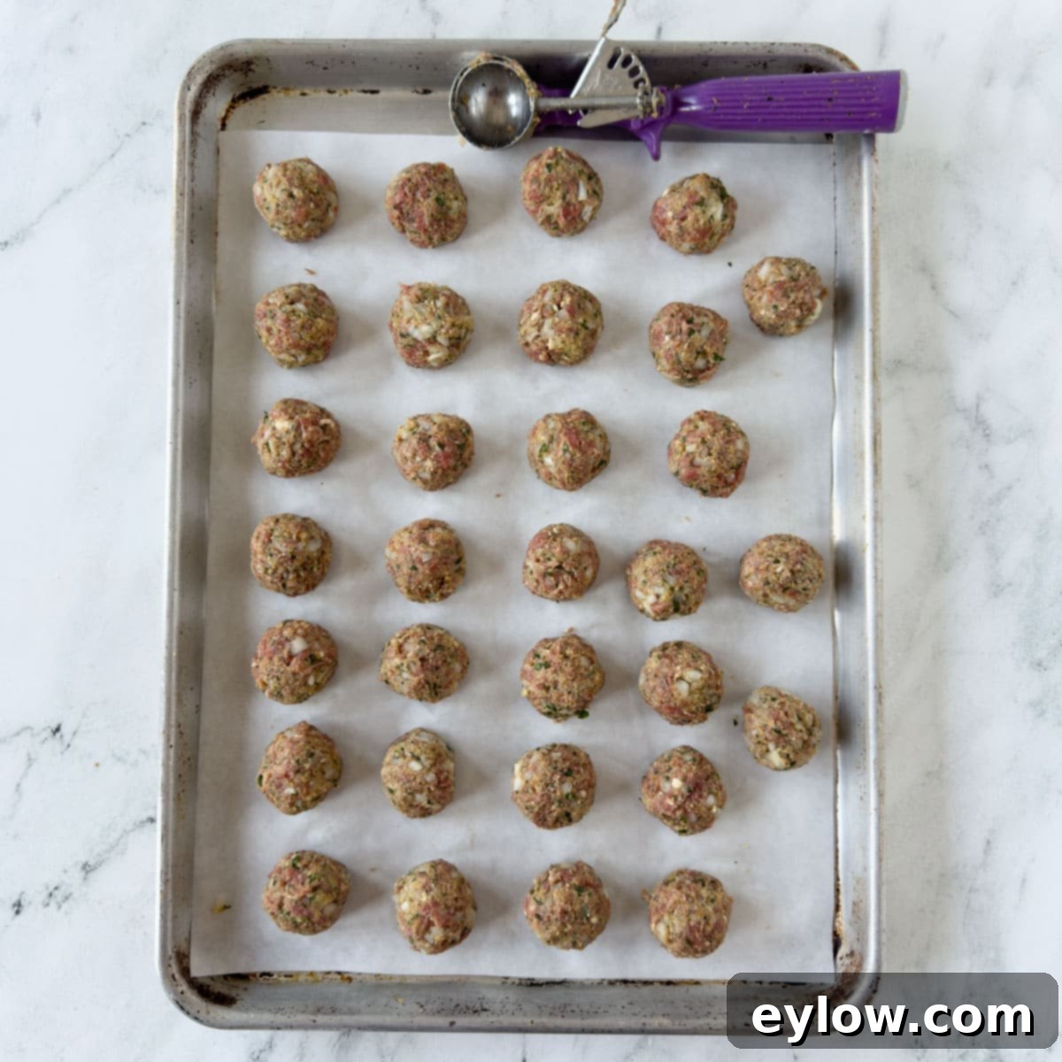 Portioned meatballs on a parchment baking sheet with a disher.