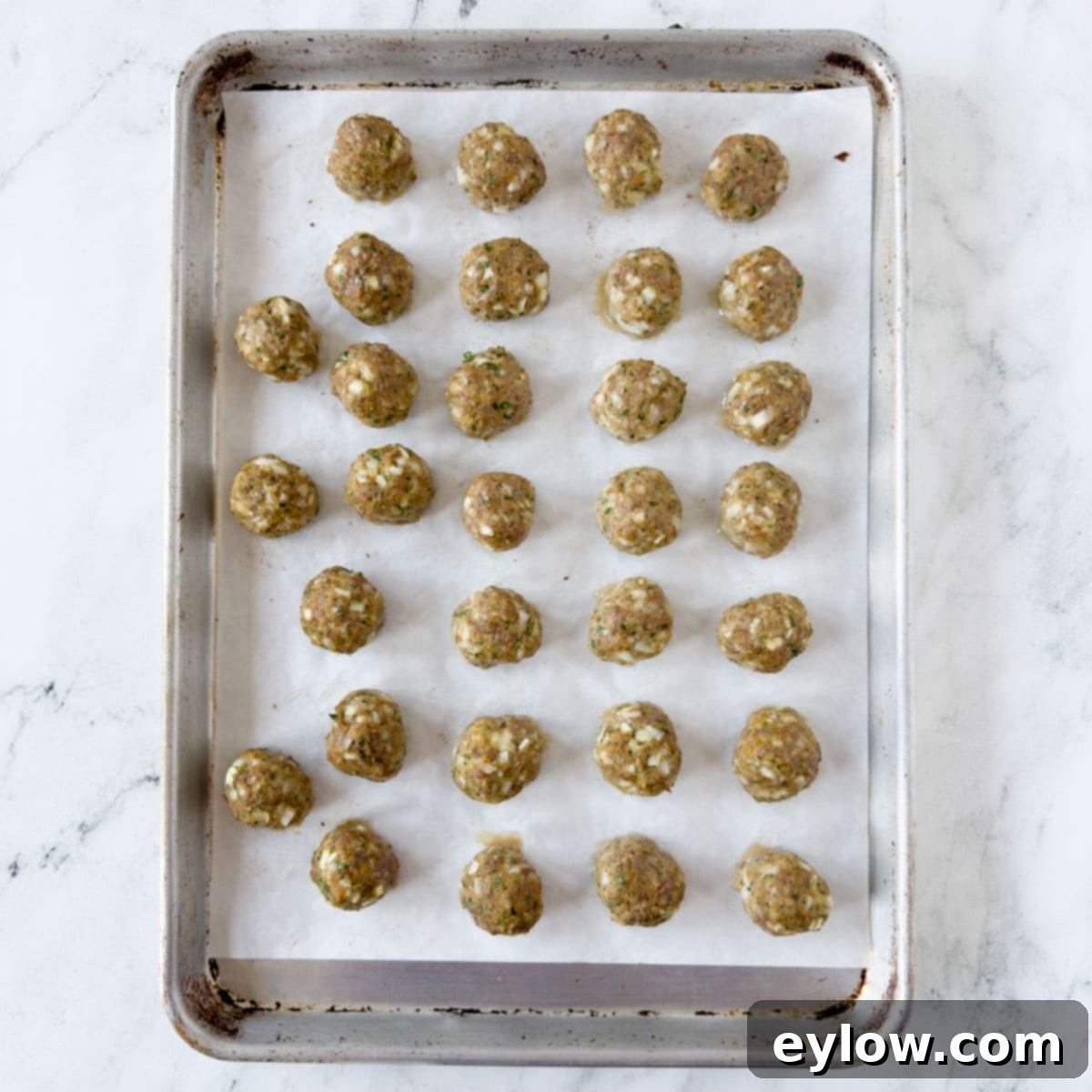 Baked beef meatballs on a rimmed baking sheet on a marble counter.