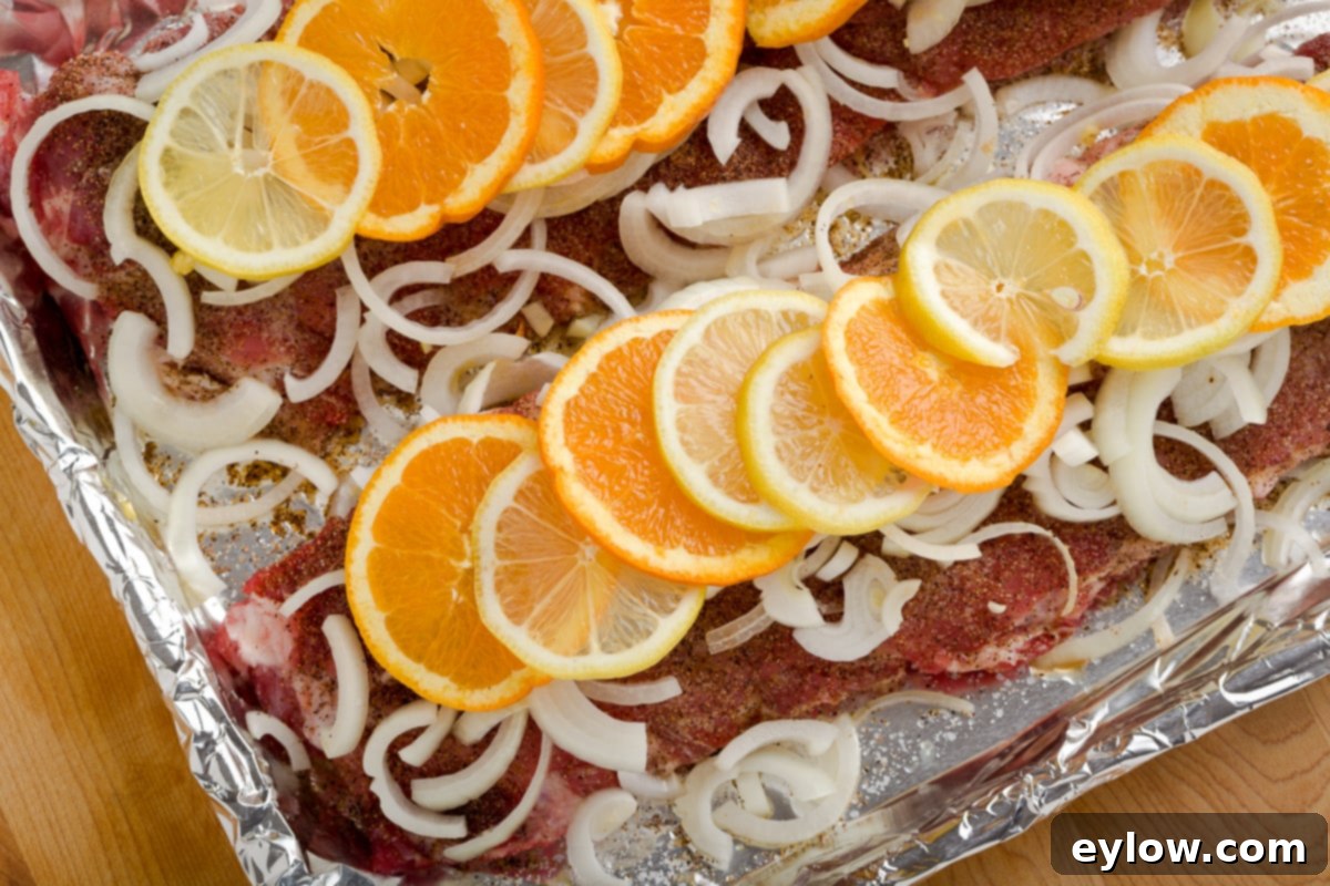 Baby back ribs covered in slice onions, lemons and orange on foil tray.