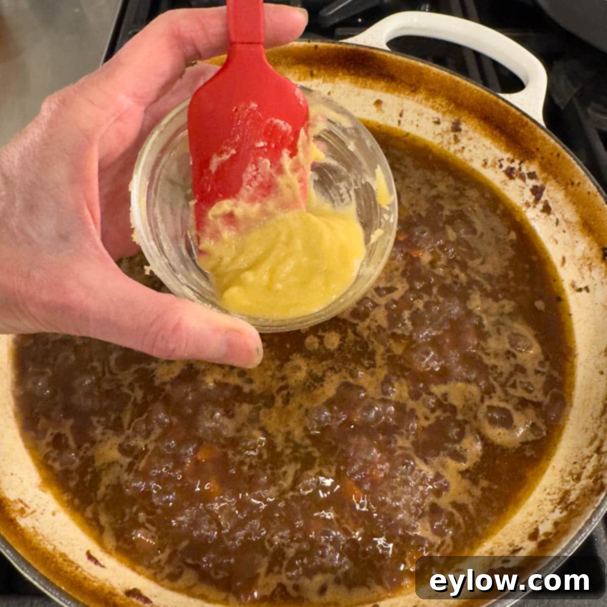 Butter and flour mixture being added to a red wine pan sauce for thickening.