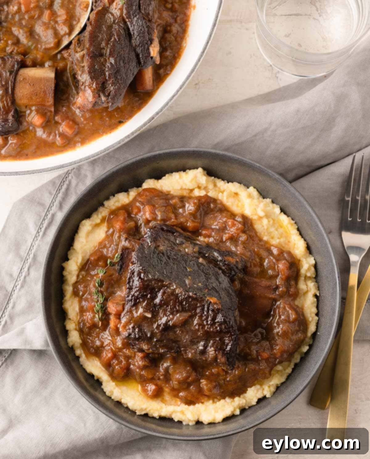 A gray bowl with creamy polenta topped with braised beef short ribs and sauce.