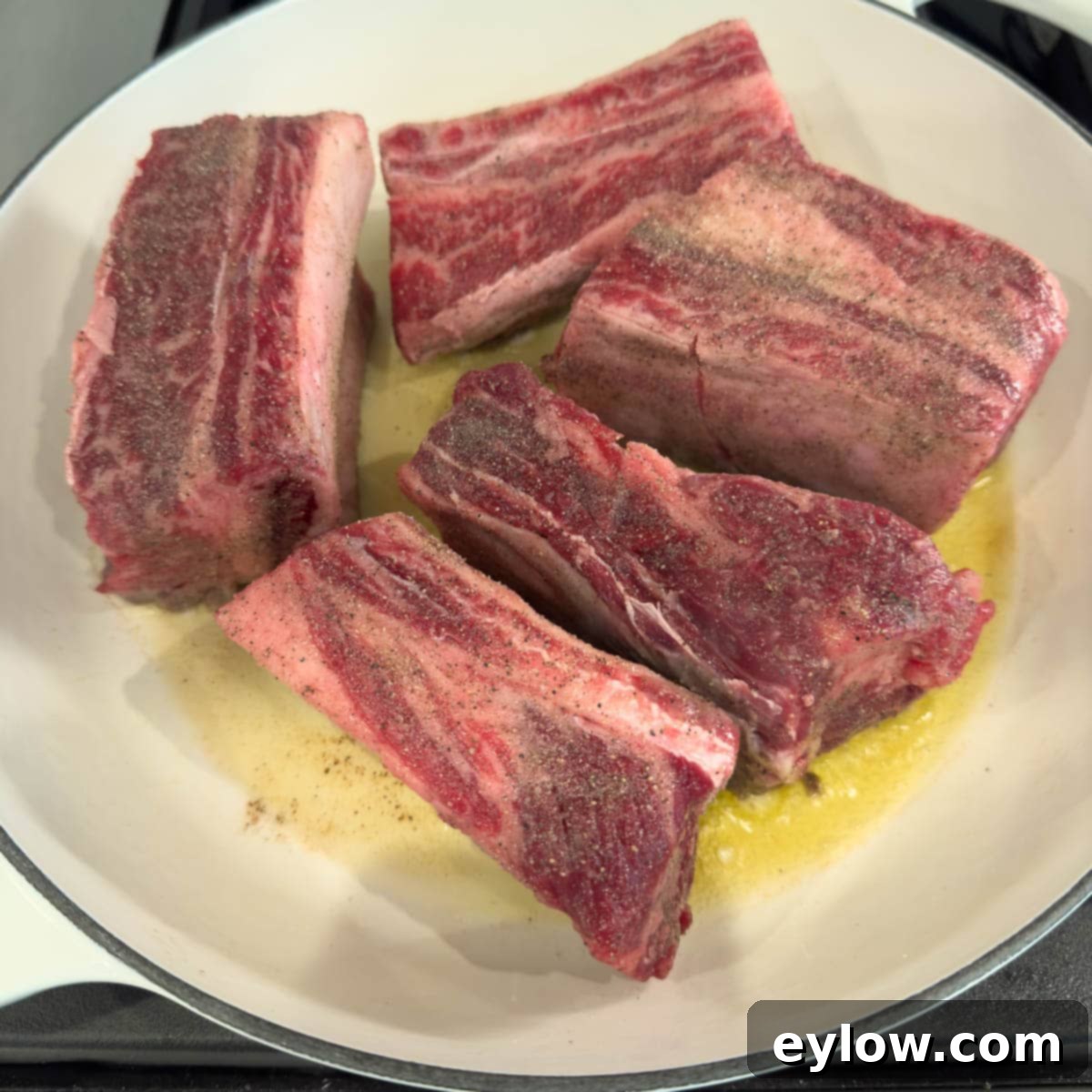 Raw beef short ribs being browned in a wide casserole called a braiser.