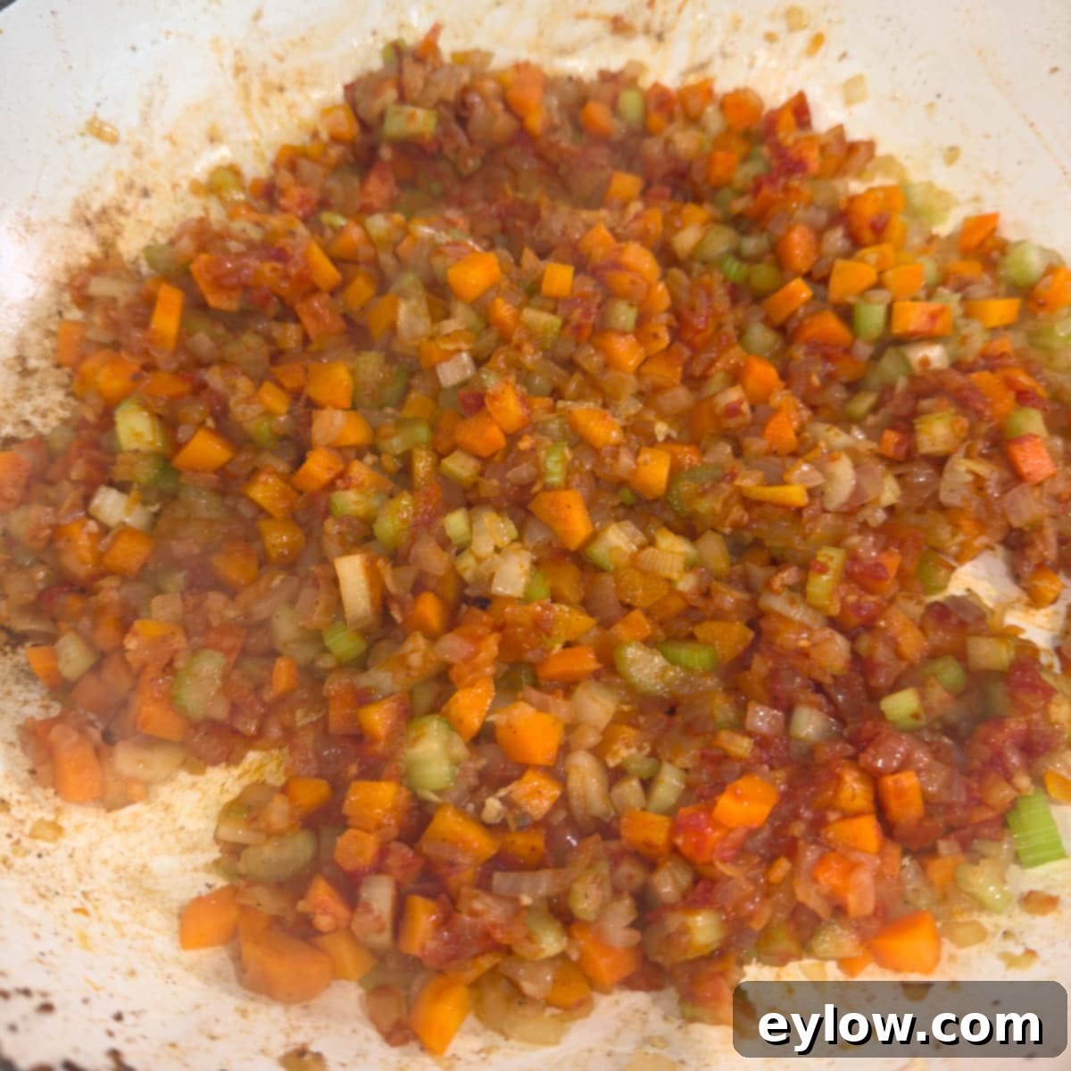 Cooking carrot, onion, and celery with tomato paste in a wide pan.
