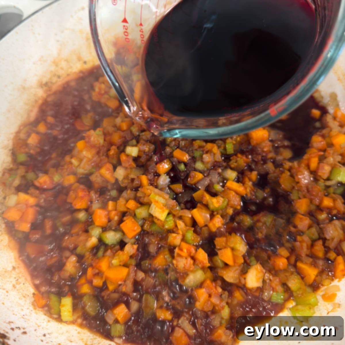 Pouring dark red wine into a pan with cooking vegetables for a reduction sauce.
