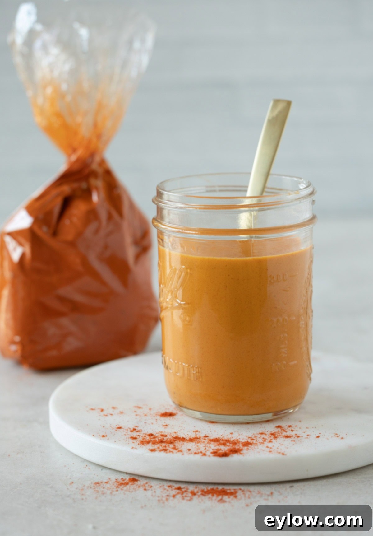 A jar of vivid orange paprika sauce with a gold spoon and paprika sprinkled on the table.