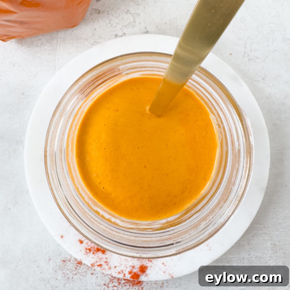 Vivid orange paprika sauce in a jar with a gold spoon and sprinkles of red paprika on the plate. 