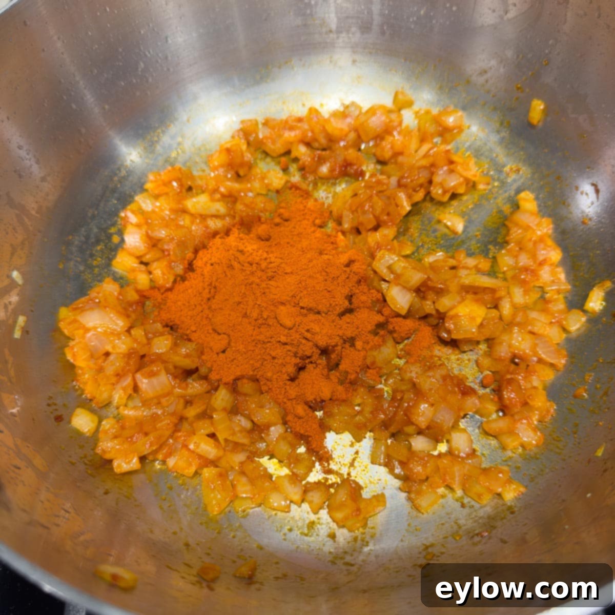 Paprika added to a pan of cooking onions turning it bright orange.