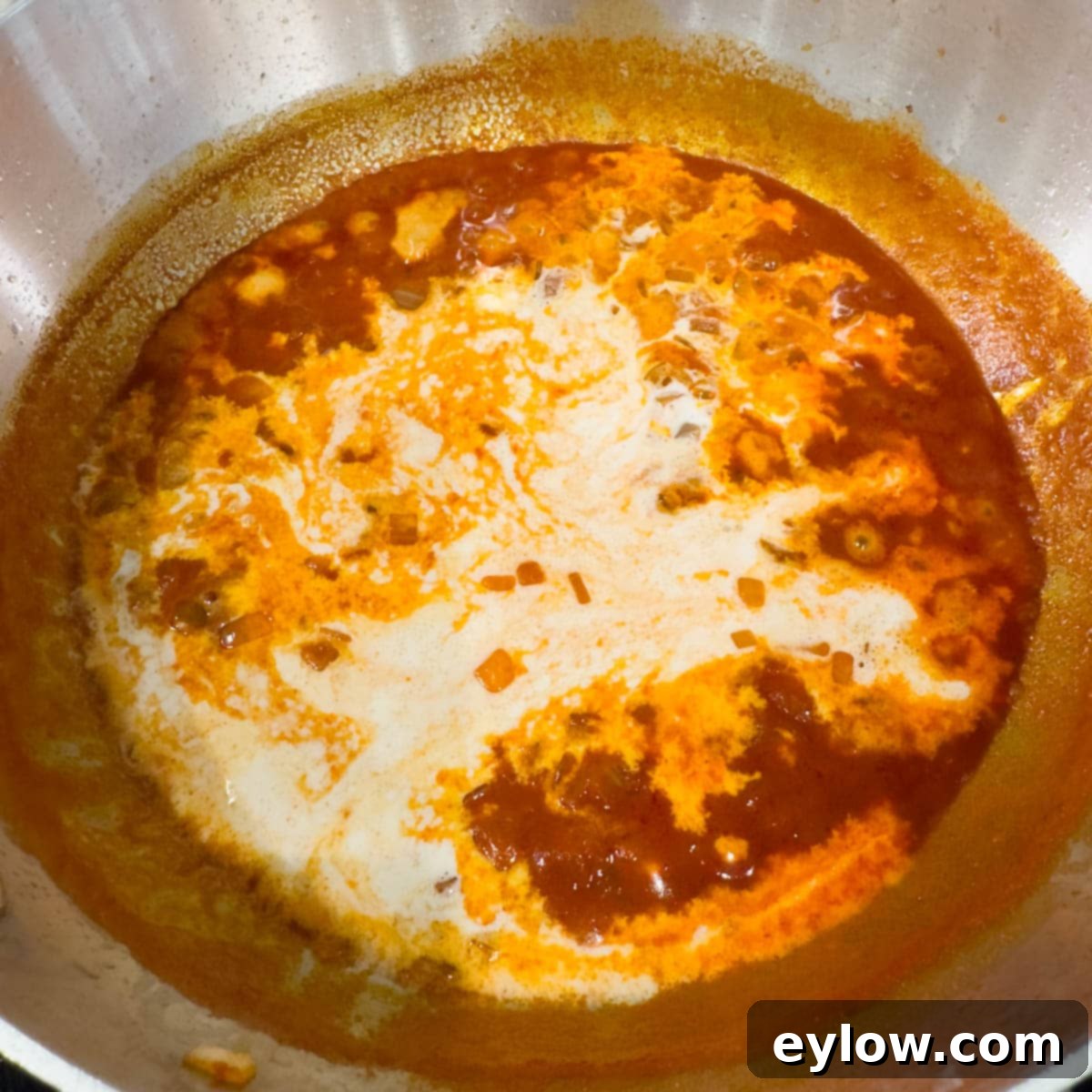 Heavy cream added to a pan of simmering red paprika sauce.