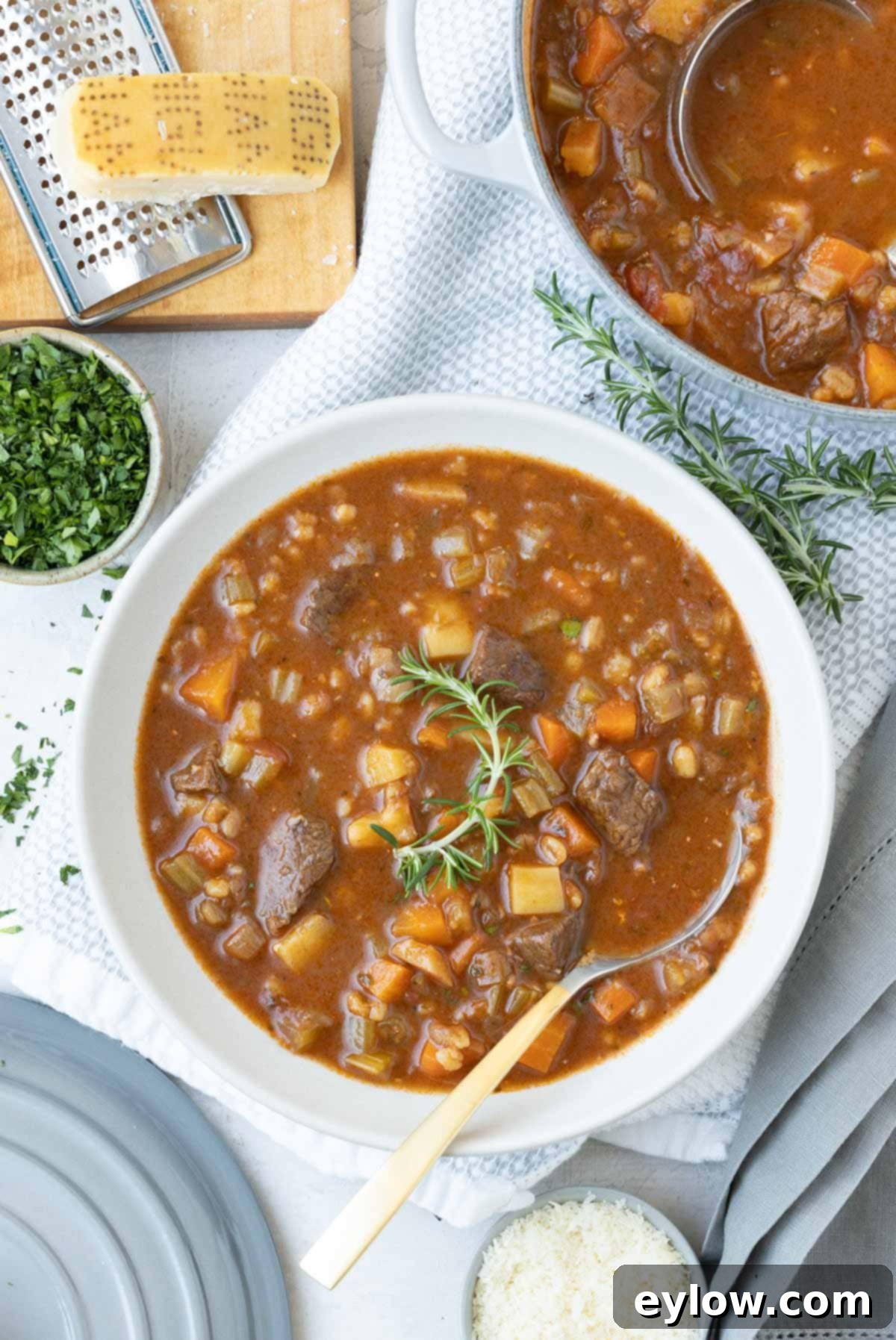 Hearty Beef, Barley & Vegetable Soup 2 A steaming bowl of hearty beef barley vegetable soup garnished with fresh rosemary.