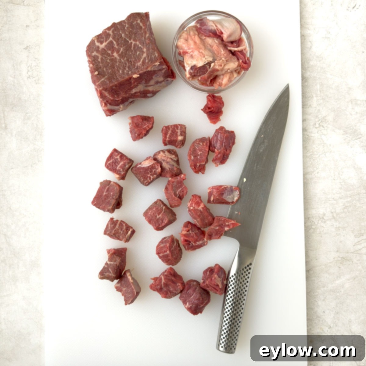 Hearty Beef, Barley & Vegetable Soup 4 Slicing boneless beef chuck roast into 1-inch cubes on a white cutting board.