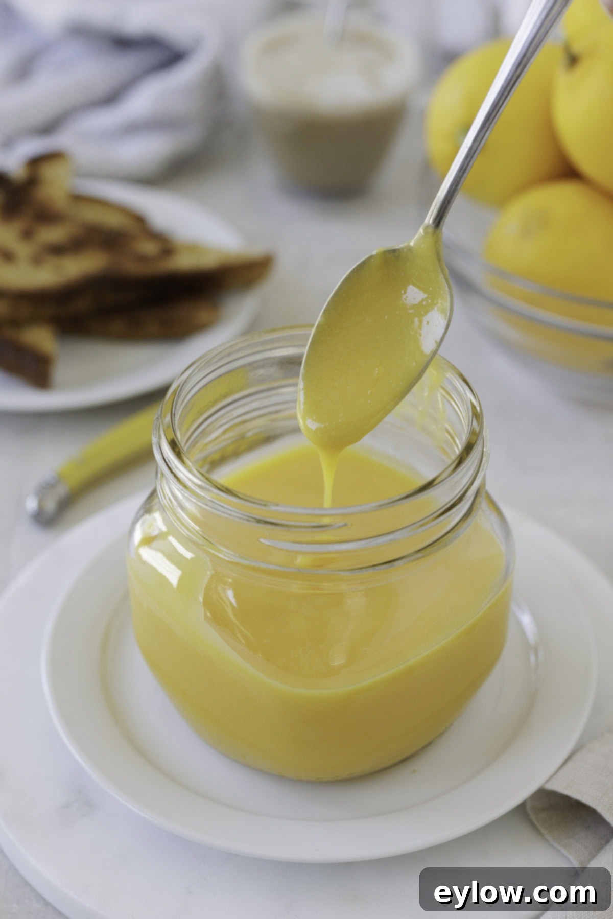Creamy sugar-free lemon curd dripping from a silver spoon over a jar, highlighting its luscious texture.
