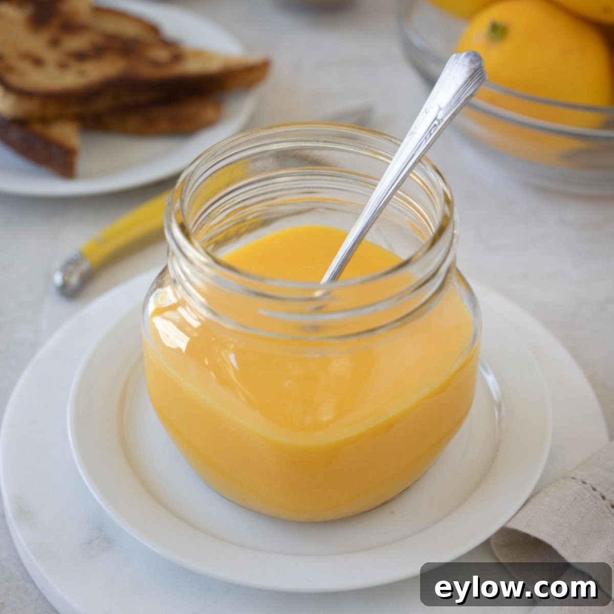A beautiful glass jar filled with bright yellow sugar-free lemon curd, accompanied by a bowl of fresh, vibrant lemons on the side.