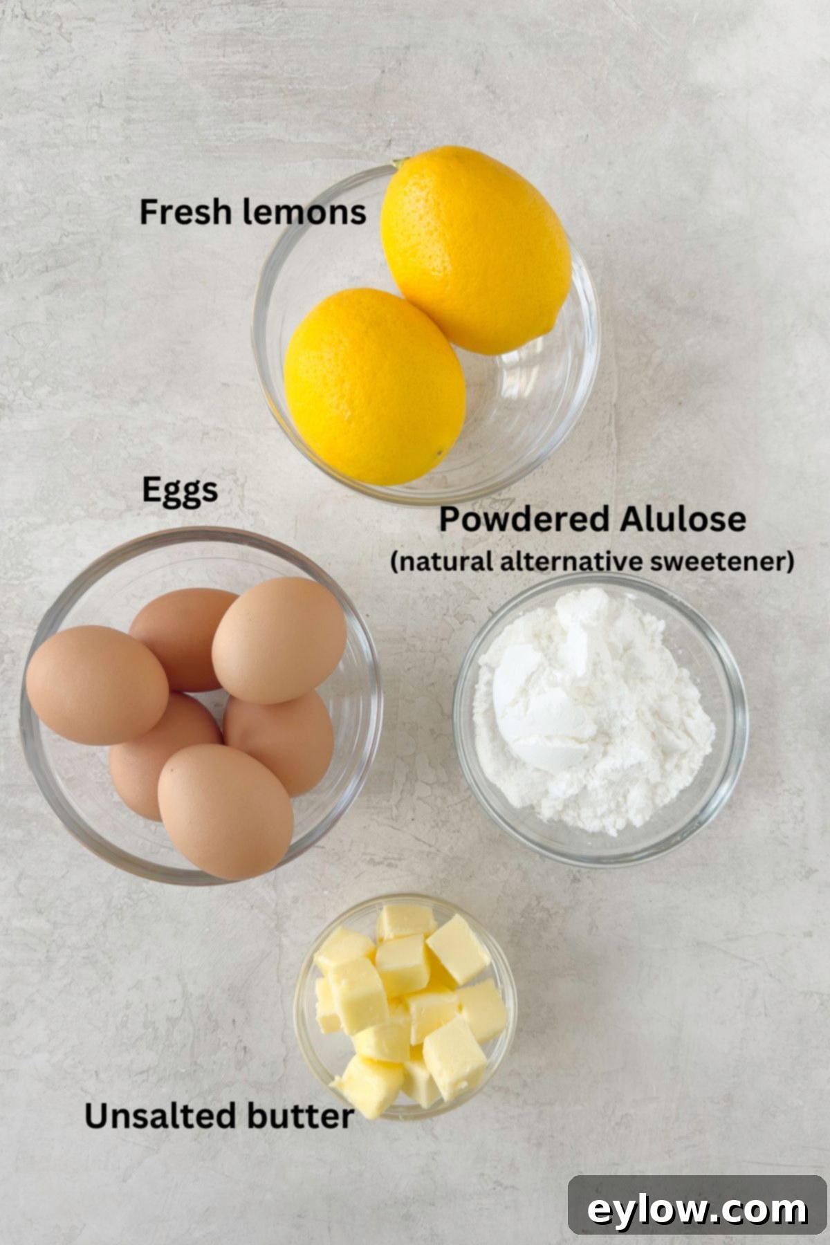 Simple ingredients for sugar-free lemon curd, including fresh lemons, powdered allulose, eggs, and unsalted butter, neatly arranged on a kitchen counter.