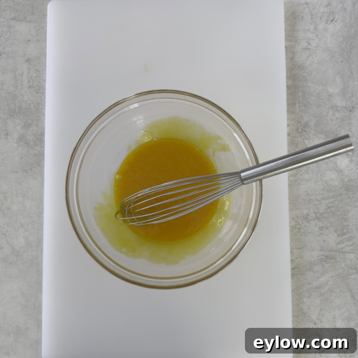 Bright golden yellow egg yolks, perfectly whisked until smooth, in a clear glass bowl, ready for tempering.