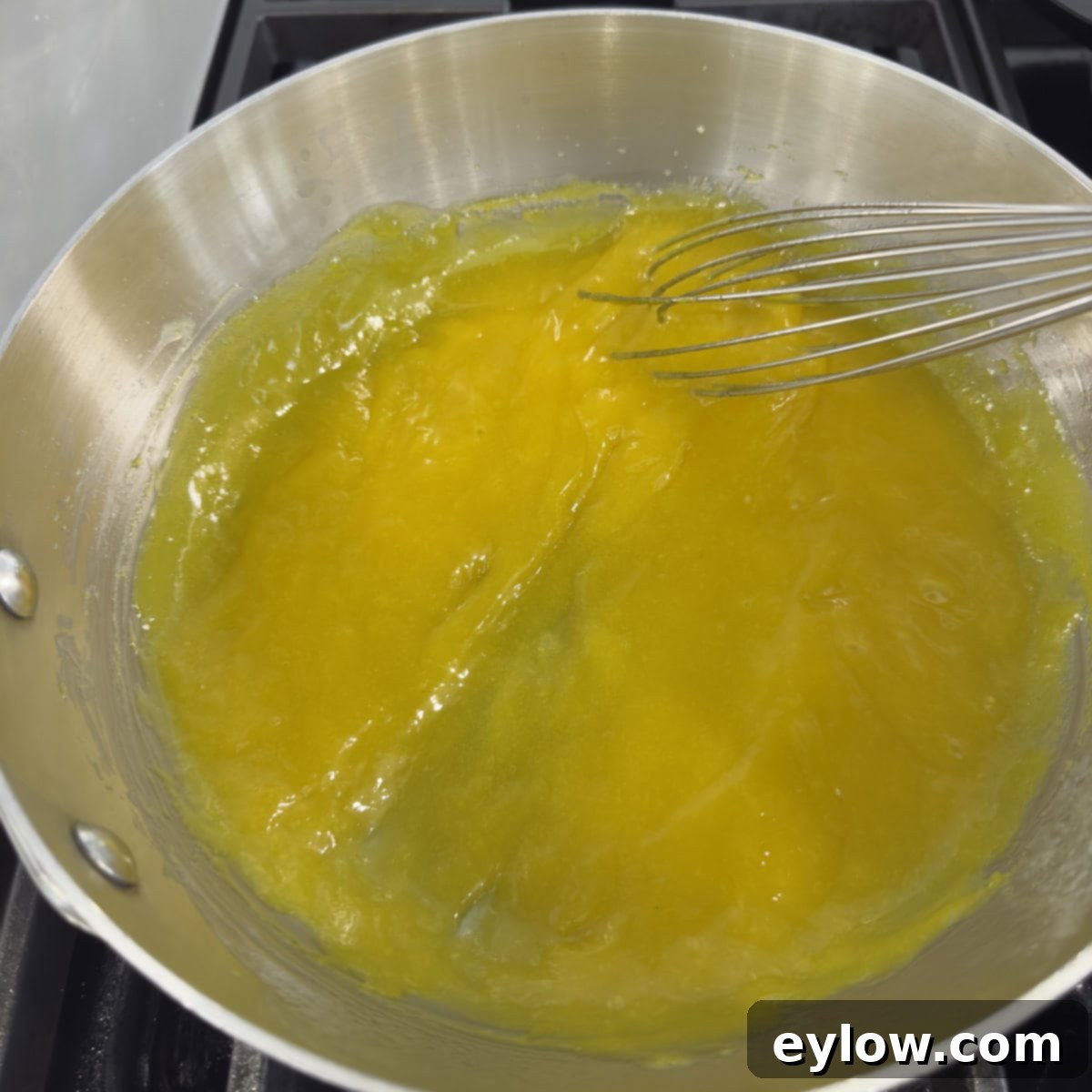 Thickened, golden cooked lemon curd coating the back of a spoon, signaling it's ready to be strained from the saucepan.
