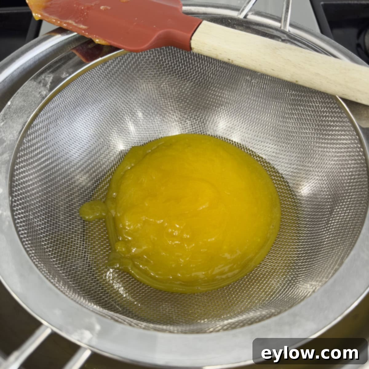 Straining freshly cooked lemon curd through a fine-mesh sieve into a clean glass bowl, ensuring a silky-smooth texture.