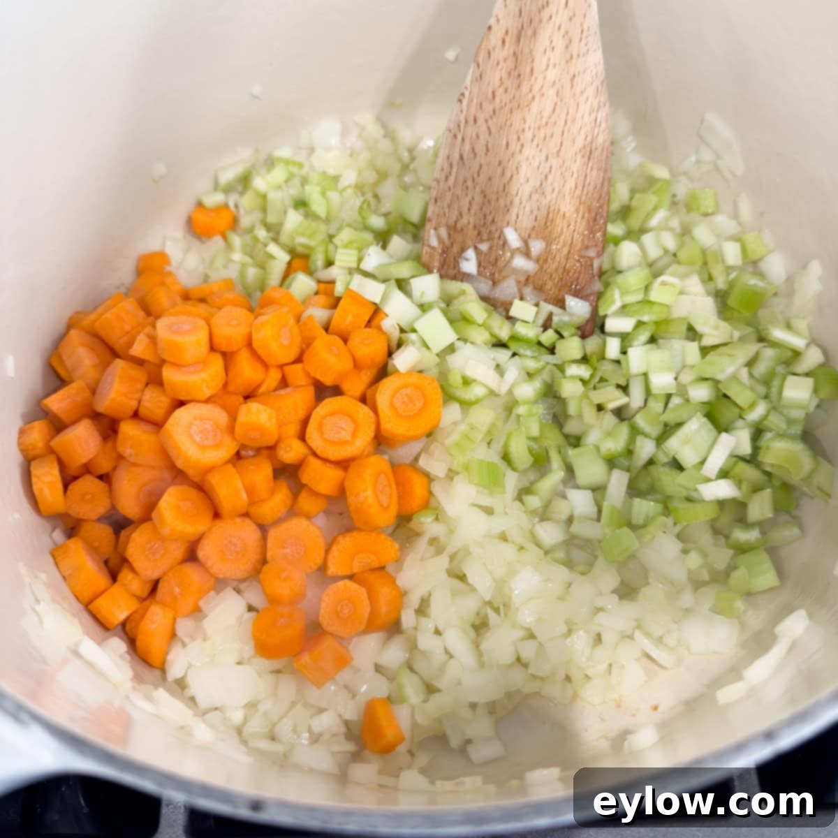 Soul-Warming Chicken Minestrone 5 Carrots, onion, and celery in a pot for soup with a wood spatula.