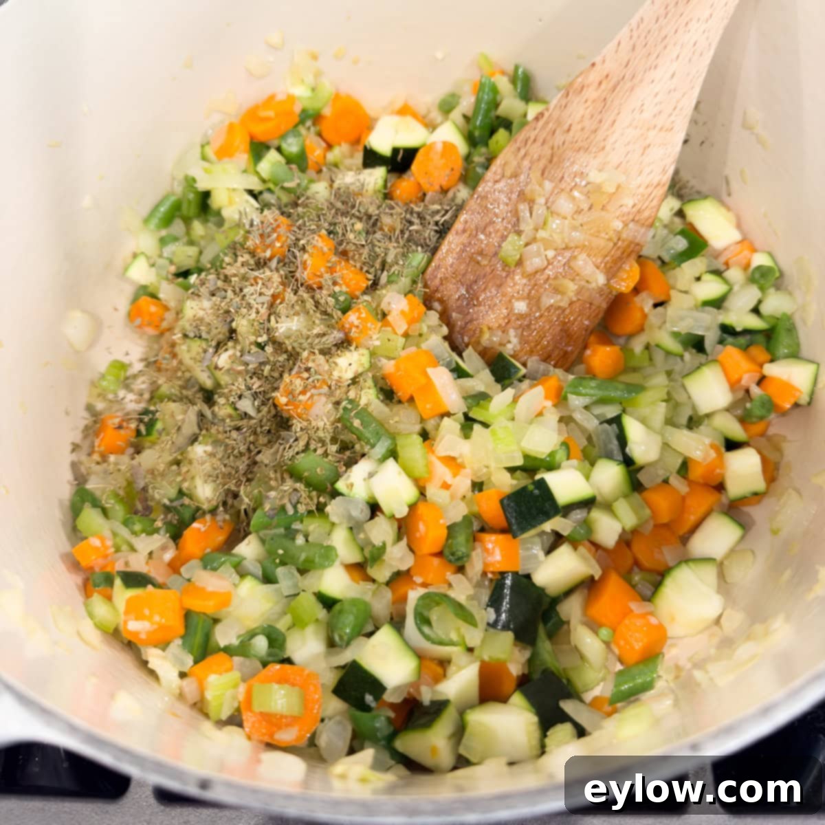 Soul-Warming Chicken Minestrone 6 Mixed vegetables for soup in a stock pot with a wooden spatula.