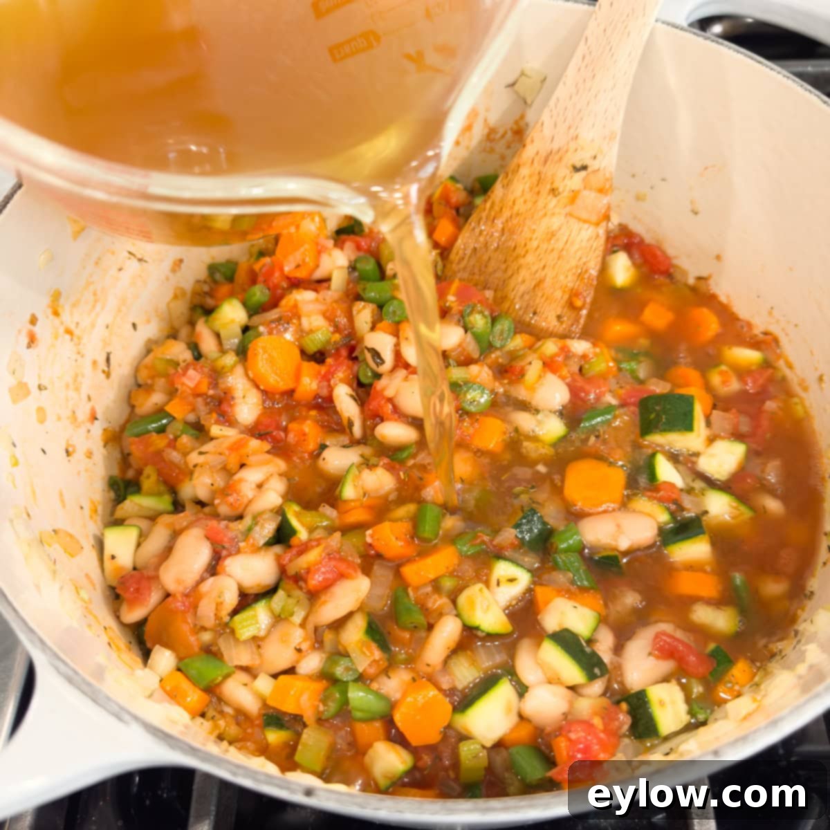 Soul-Warming Chicken Minestrone 8 Golden chicken broth pouring into a pot of chicken vegetable soup.