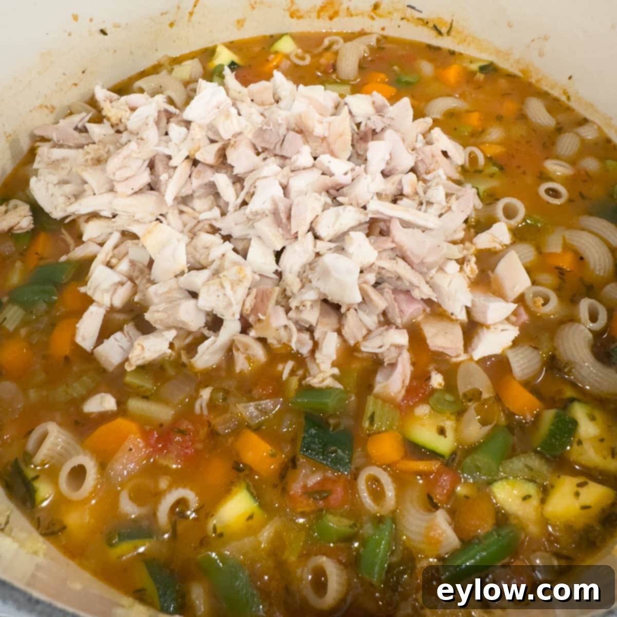 Soul-Warming Chicken Minestrone 9 A pot of soup in process showing vegetables, broth, and shredded chicken.