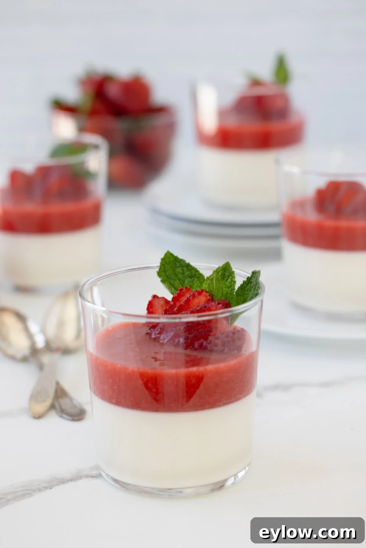 Velvety Strawberry Panna Cotta with Sweet Berry Drizzle 2 Dessert glass of vanilla panna cotta topped with bright red strawberry sauce and berries.