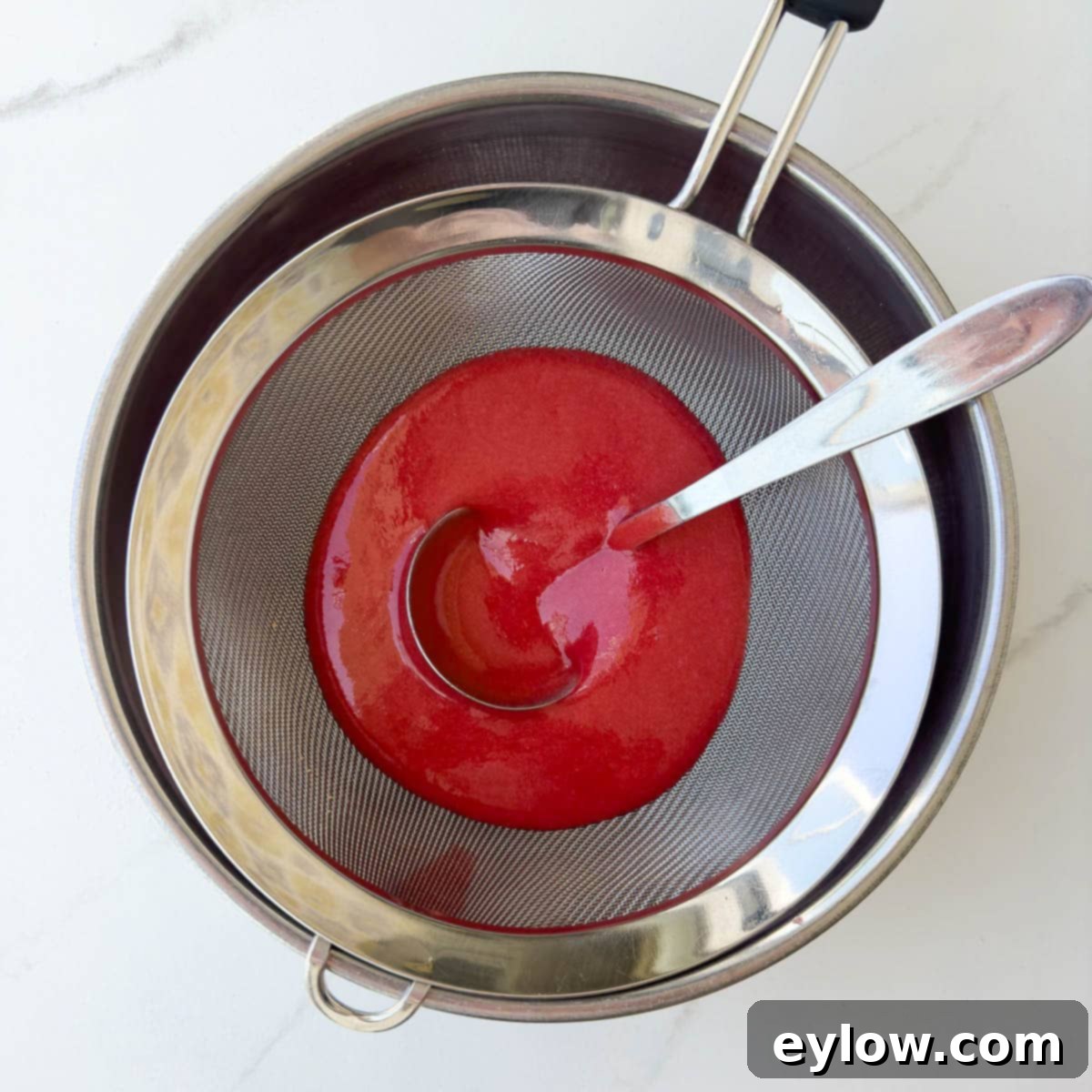 Velvety Strawberry Panna Cotta with Sweet Berry Drizzle 11 Straining strawberry puree through a fine sieve to remove seeds with a ladle.