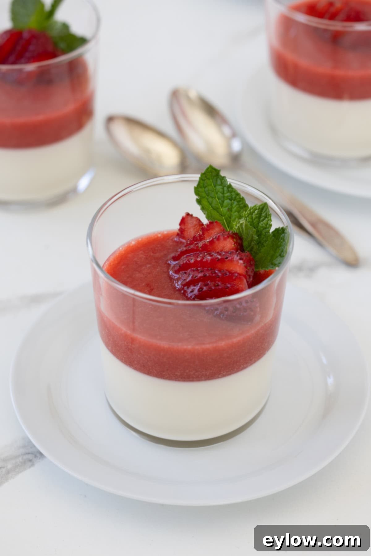 Velvety Strawberry Panna Cotta with Sweet Berry Drizzle 12 A glass of creamy vaniilla panna cotta with strawberries, berry sauce, and mint.