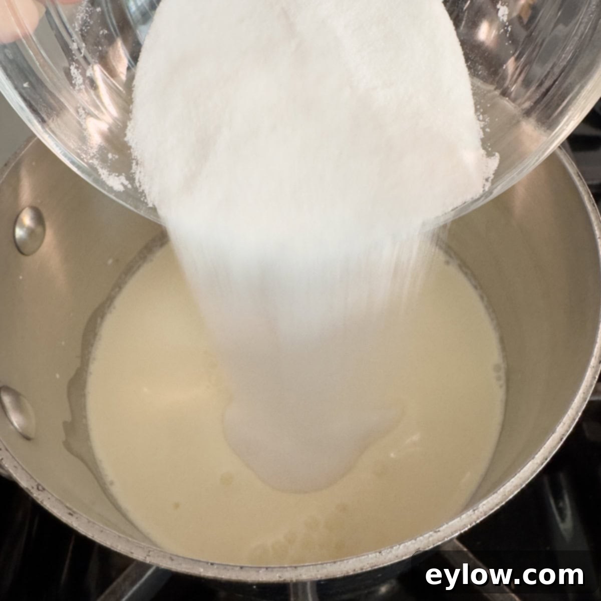Velvety Strawberry Panna Cotta with Sweet Berry Drizzle 5 Sugar pouring into a small pan on a stove top with cream.
