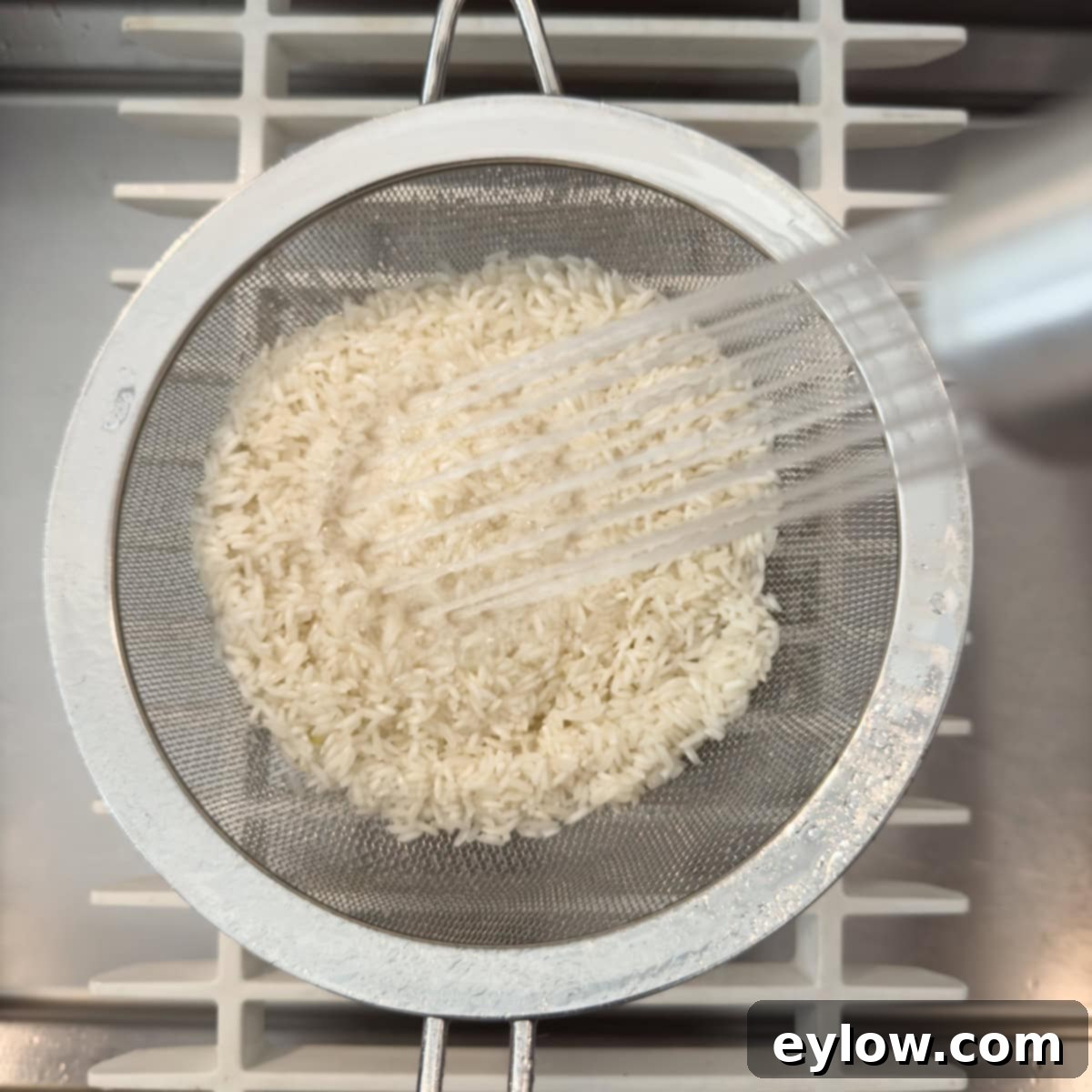 Vibrant Vegetable Rice Medley 3 White rice in a sieve being washed in the sink with a sprayer.