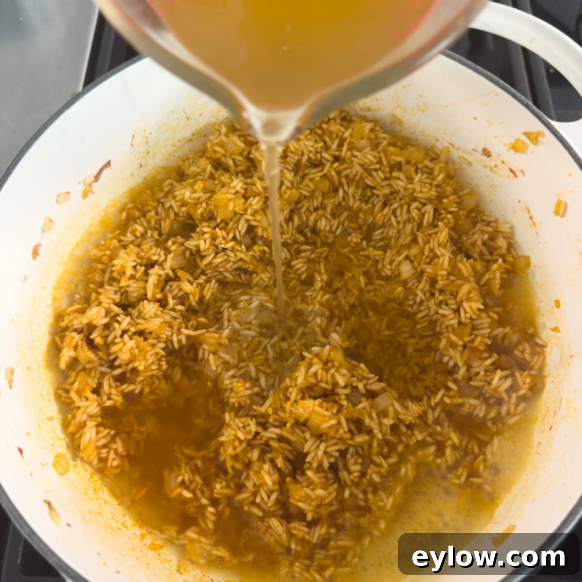 Vibrant Vegetable Rice Medley 7 Golden broth pouring into a pot of cooking rice in a heavy pot.