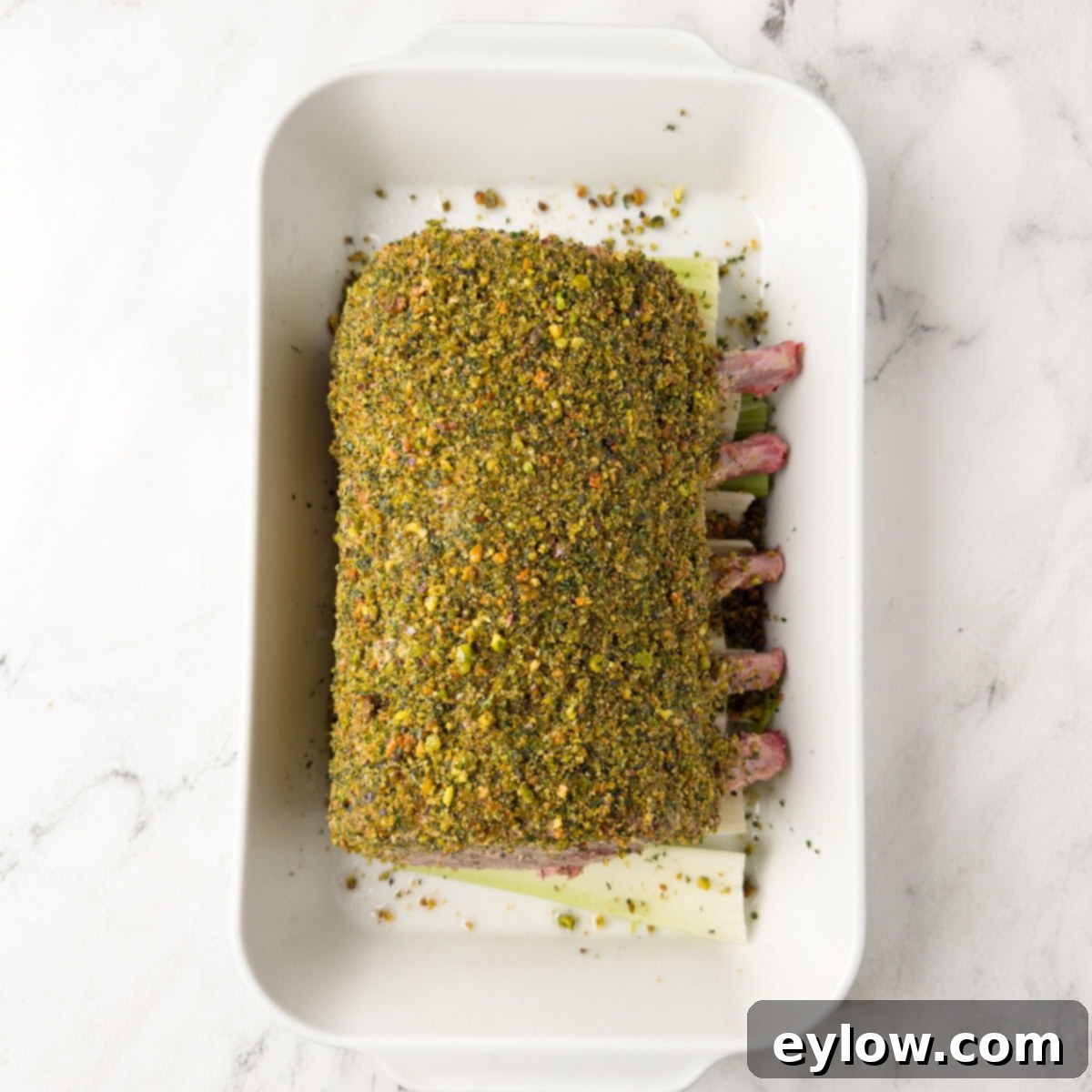 Pistachio-Encrusted Pork Rib Roast 8 A pistachio crusted pork roast ready for the oven in a white casserole dish.