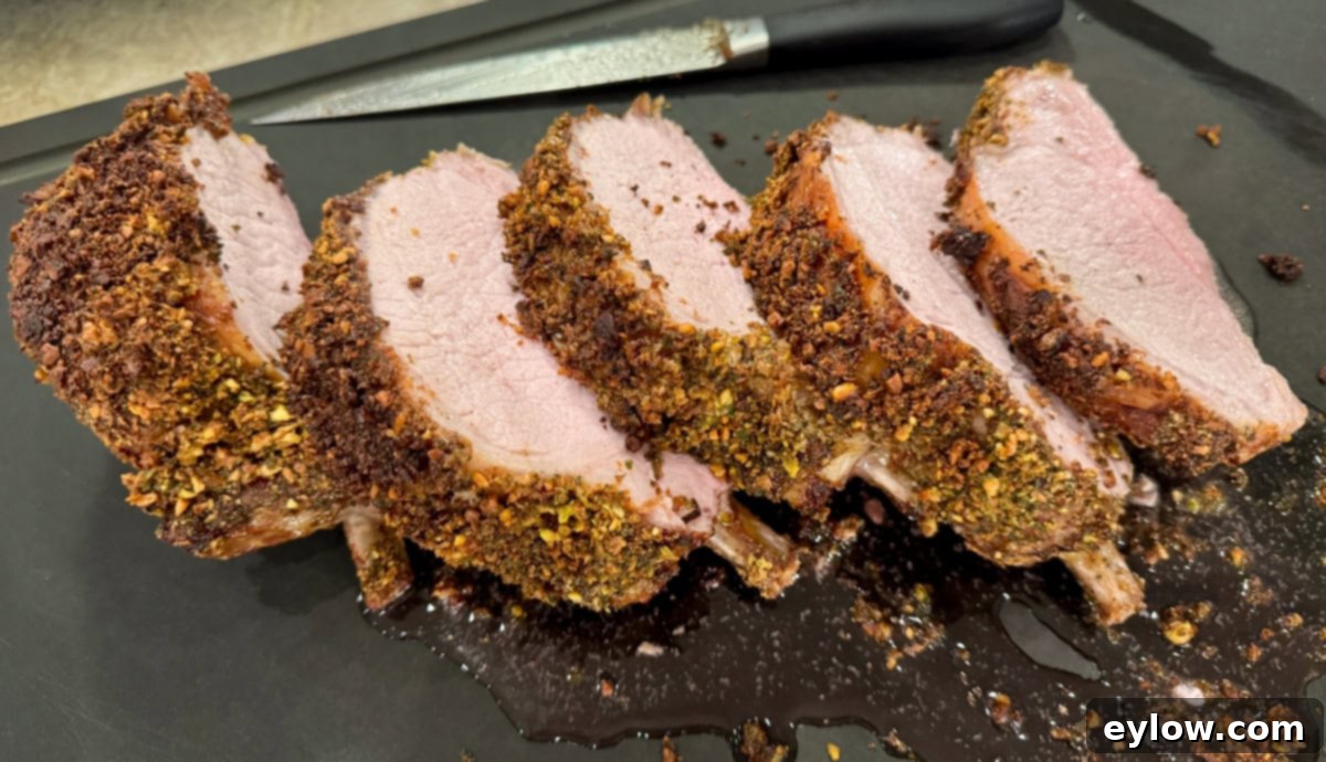 Pistachio-Encrusted Pork Rib Roast 9 Thick slices of a bone-in pork rib roast on a black cutting board with a slicing knife.