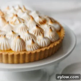 Zesty Lemon Meringue Tart 14 A beautiful lemon tart with piles of piped meringue on top of a cake plate.