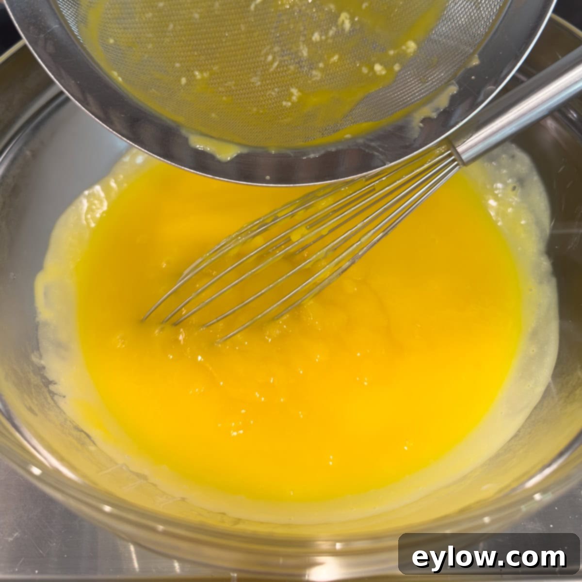 Zesty Lemon Meringue Tart 7 Straining cooked lemon curd through a fine sieve into a bowl.