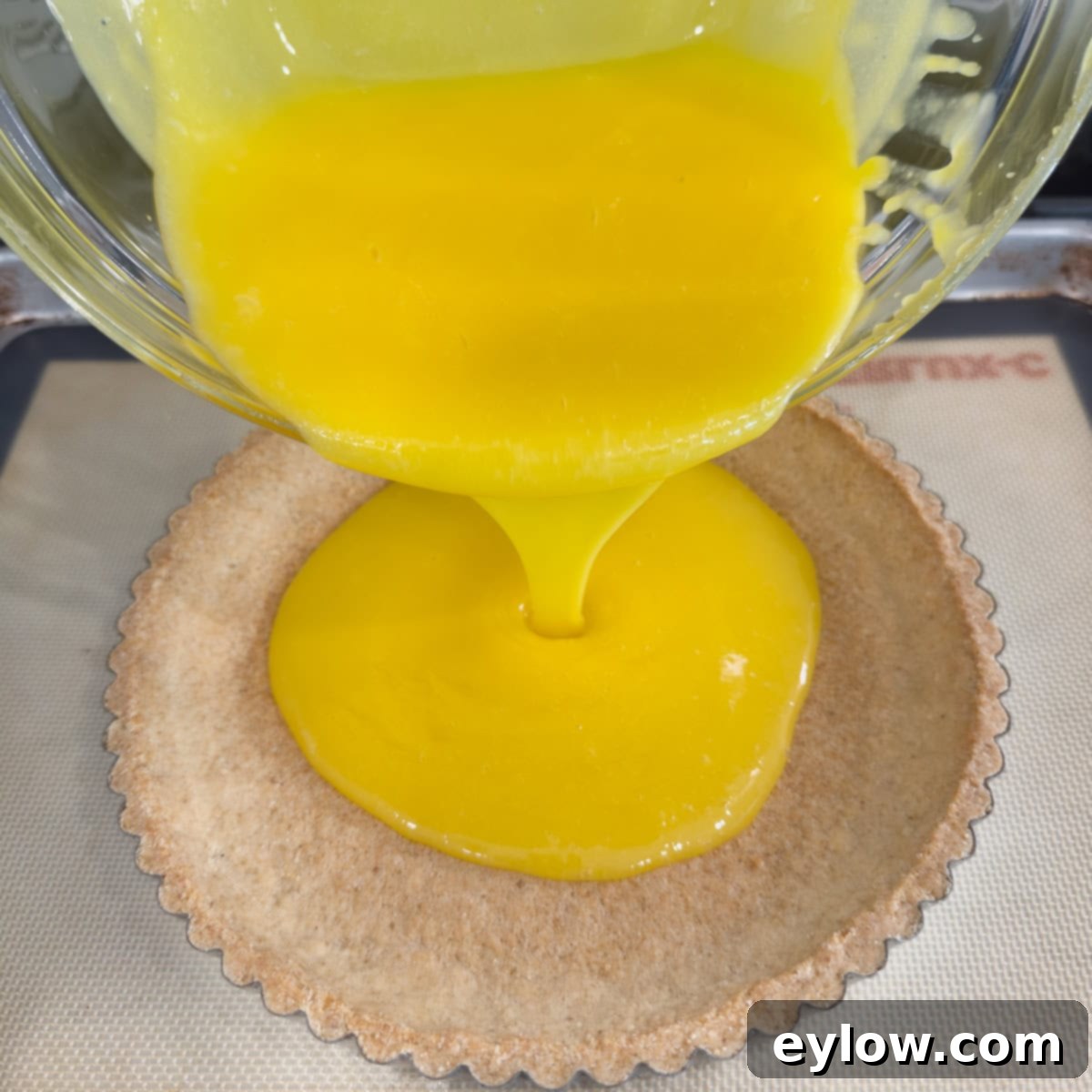 Zesty Lemon Meringue Tart 8 Pouring lemon curd from a glass bowl into a baked tart shell.